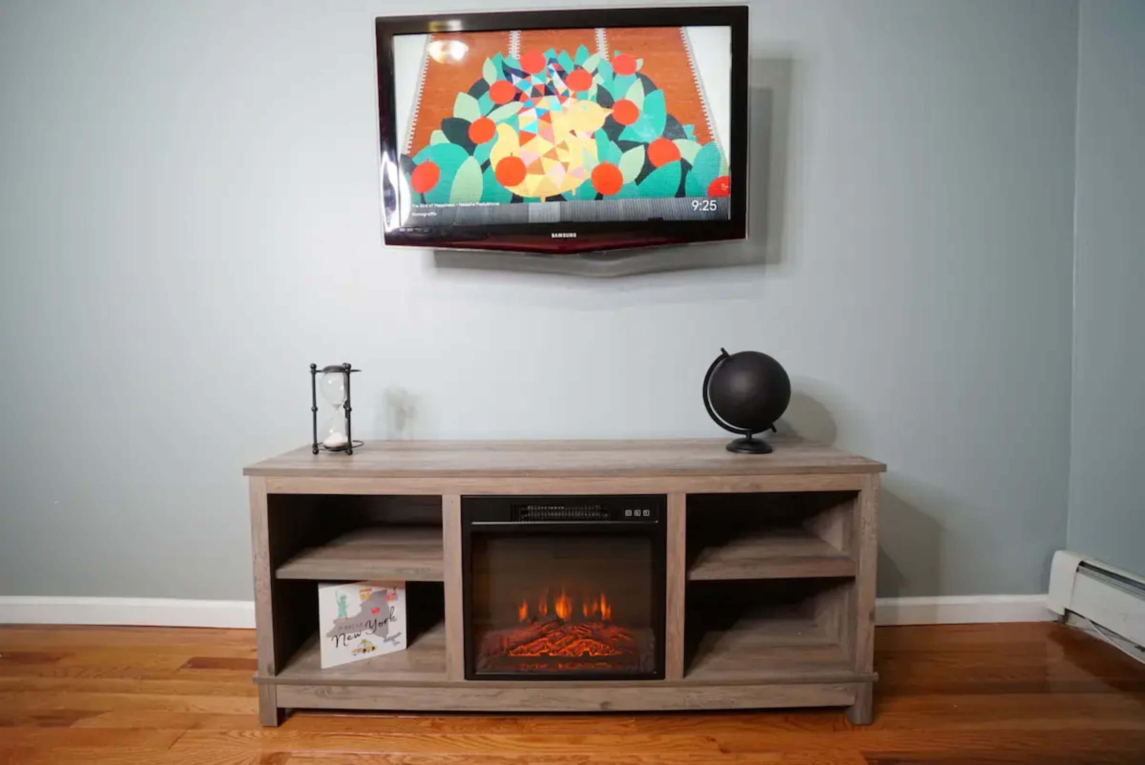 A living room setting with a wall-mounted television above a wooden entertainment unit featuring an electric fireplace and a small globe.