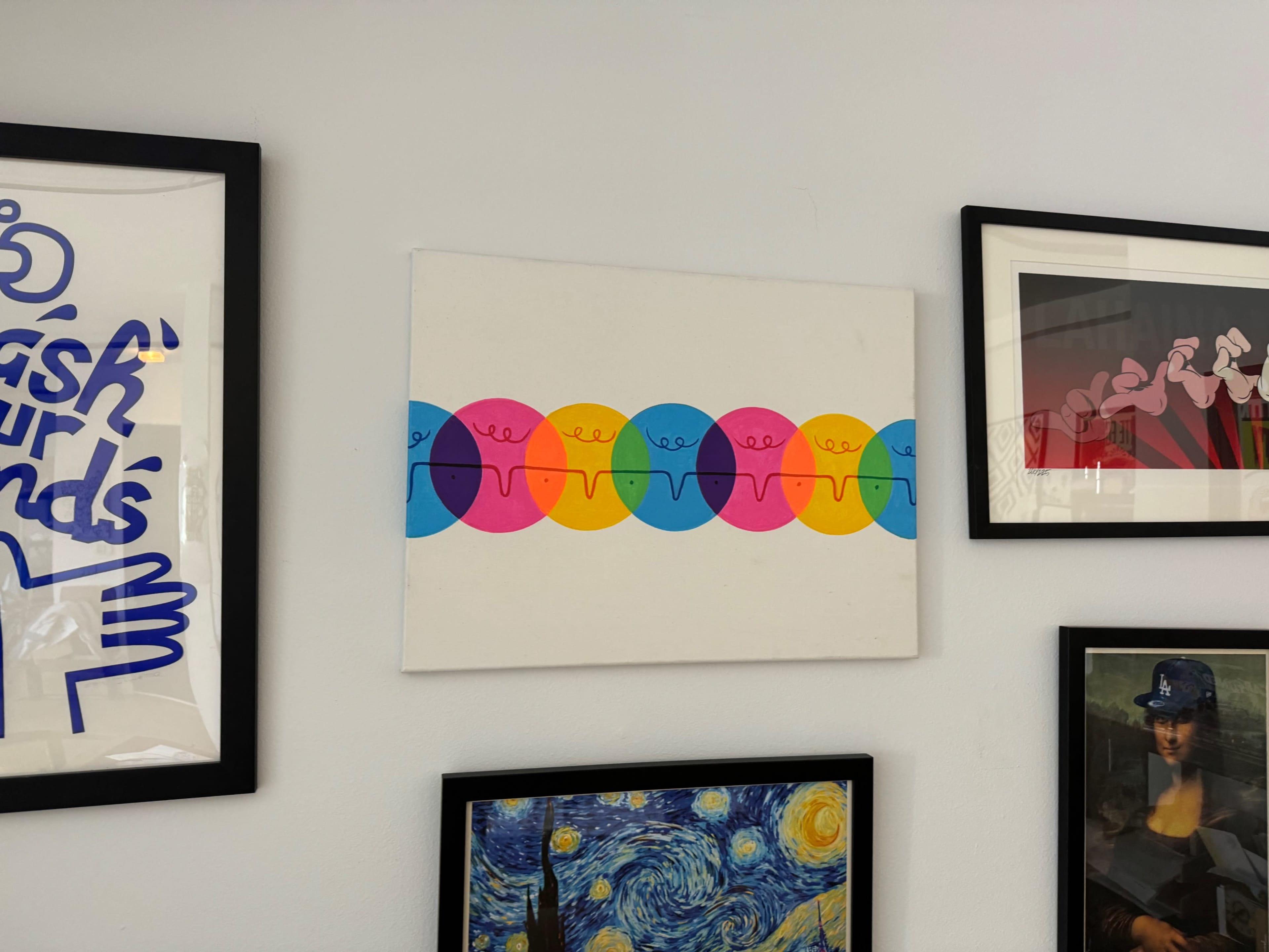 A colorful artwork featuring a row of stylized circles in pink, blue, and orange is displayed on a wall among several framed pictures.