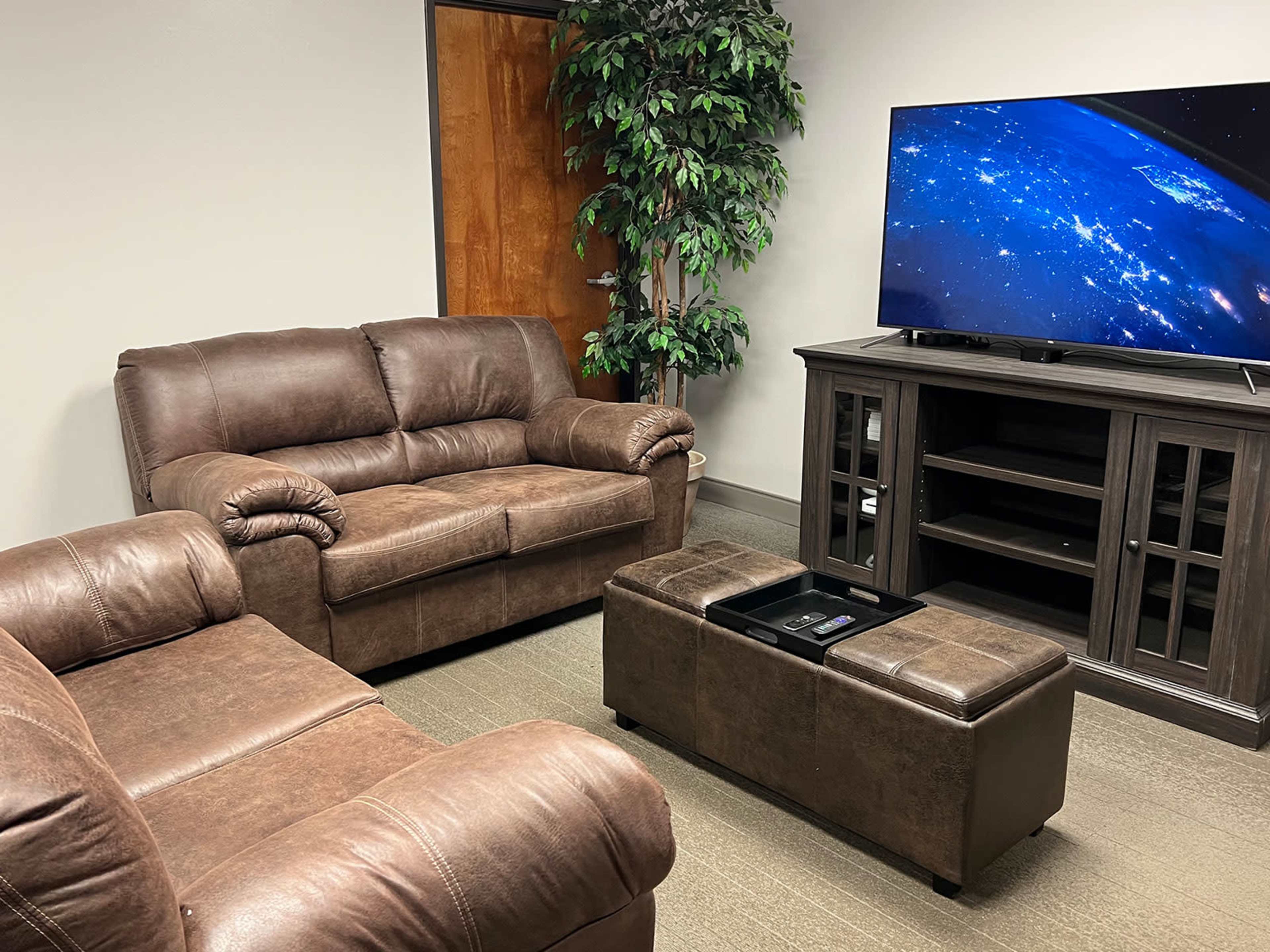 A small room furnished with two brown sofas, a coffee table, and a television mounted on a cabinet.