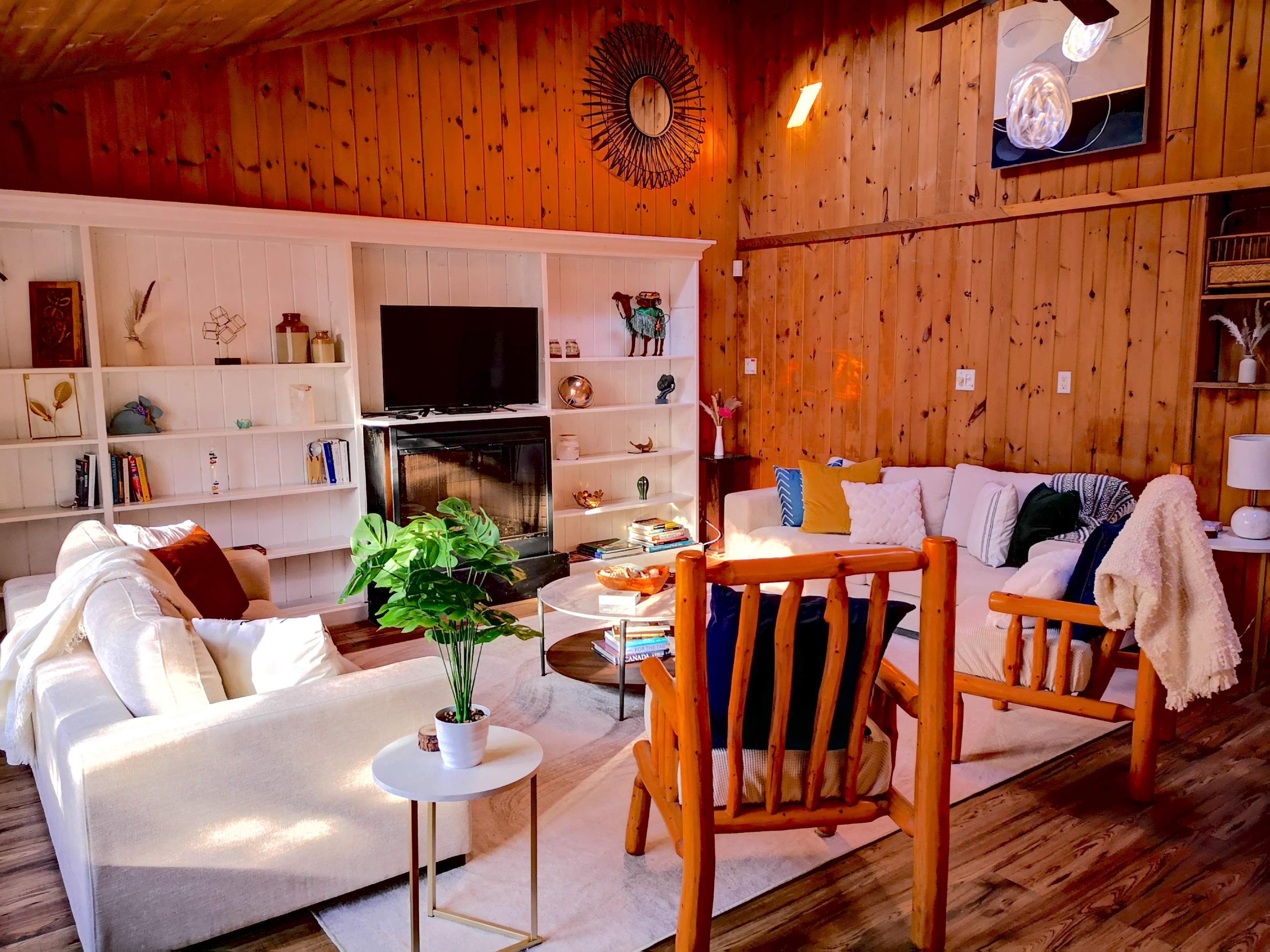 The living room features a wooden interior with a television, bookshelves, and a mix of seating arrangements including a sectional sofa and a wooden chair.