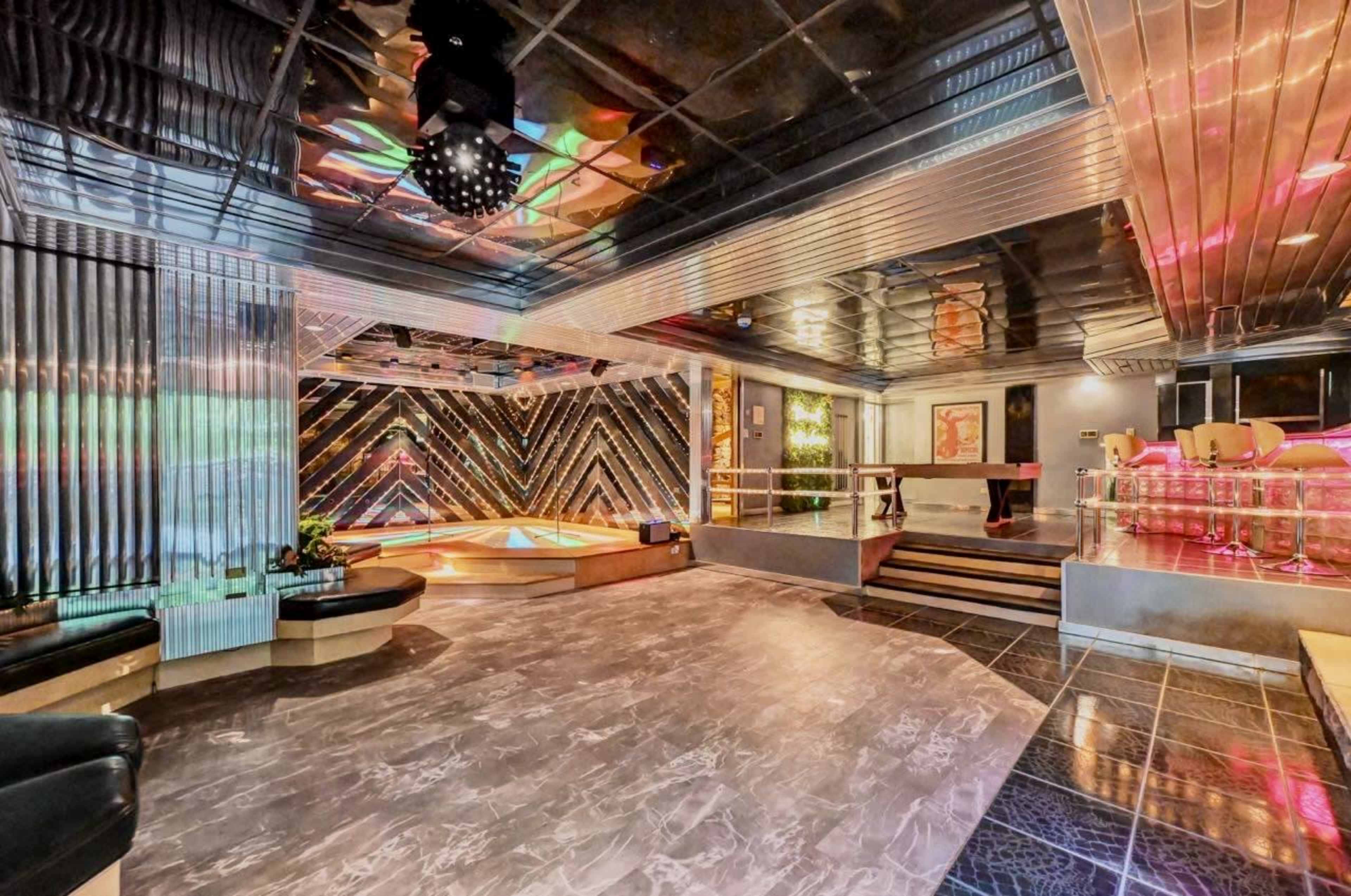 The image shows a modern interior space featuring a dance floor with colorful lighting, stylish seating areas, and a sleek ceiling design.