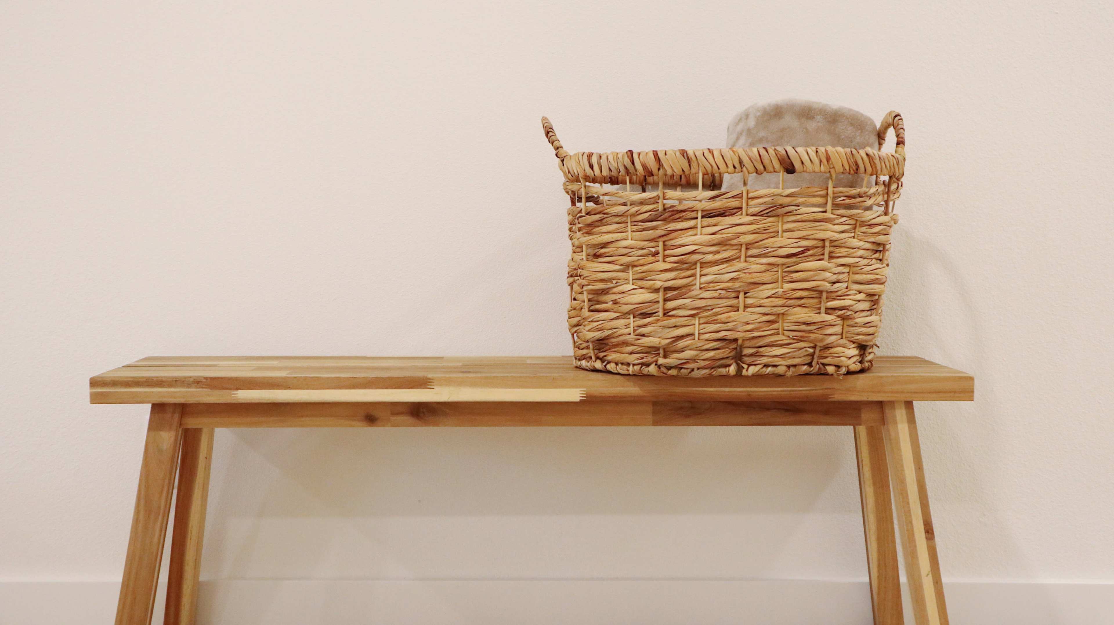 A woven basket rests on a wooden bench against a plain wall.