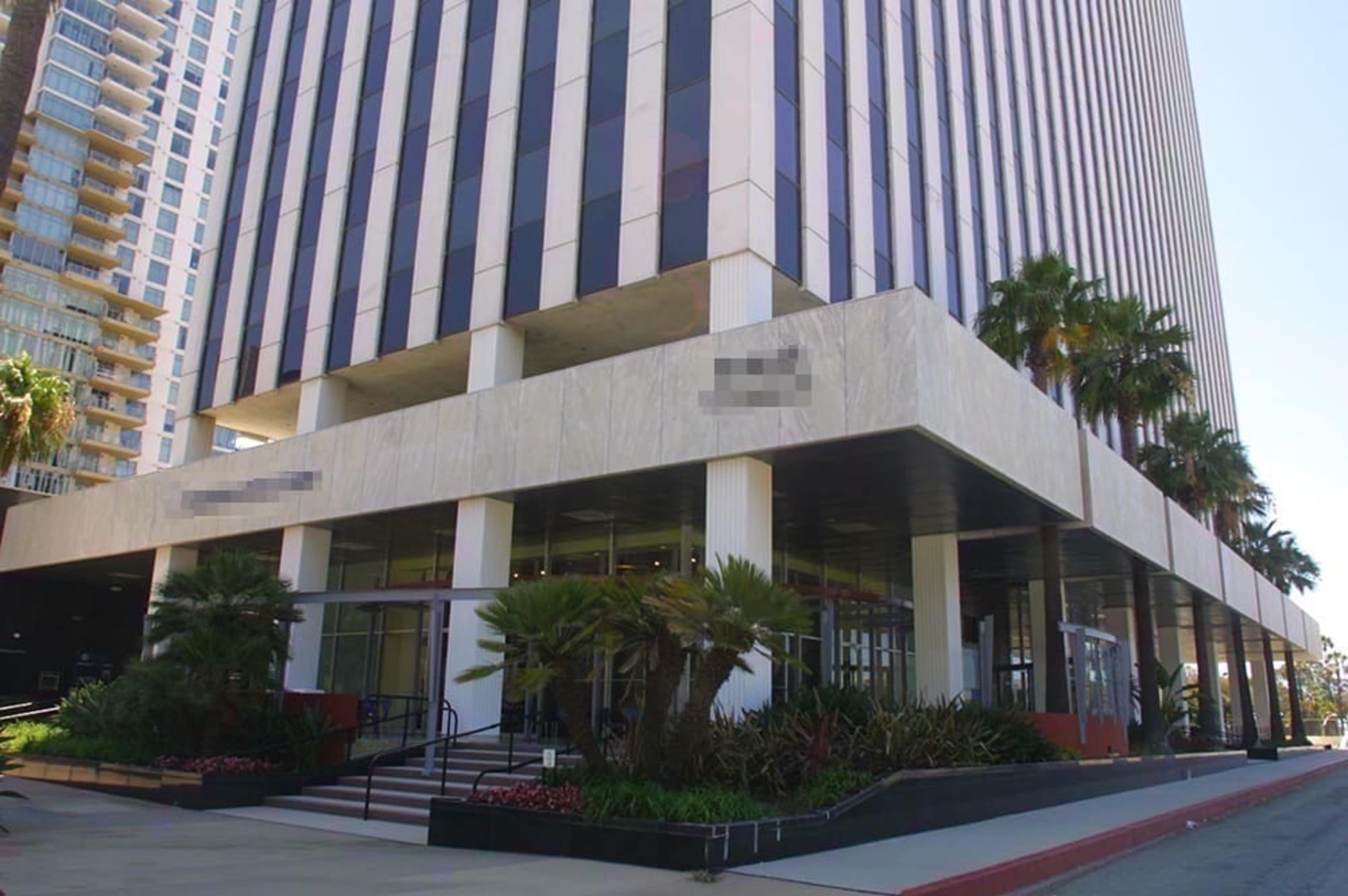 A modern office building with a marble-clad ground floor and vertical striped windows, surrounded by landscaped palm trees and plants.