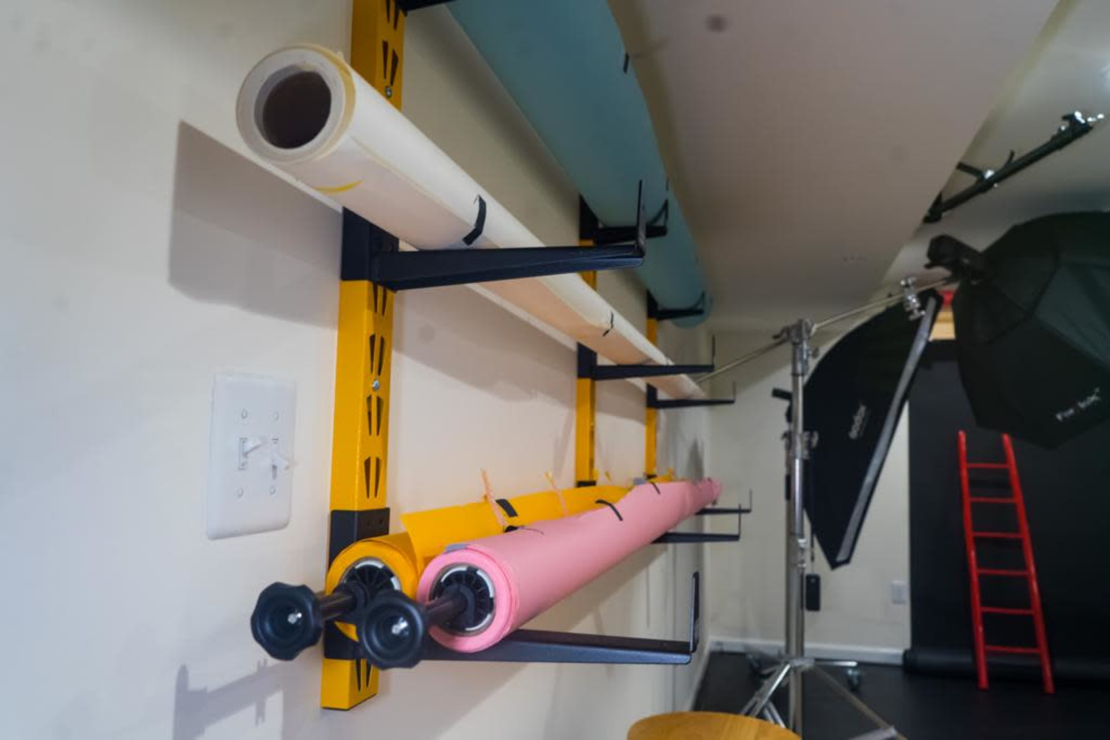 An organized wall-mounted storage system with rolls of paper in various colors and a photography backdrop setup.