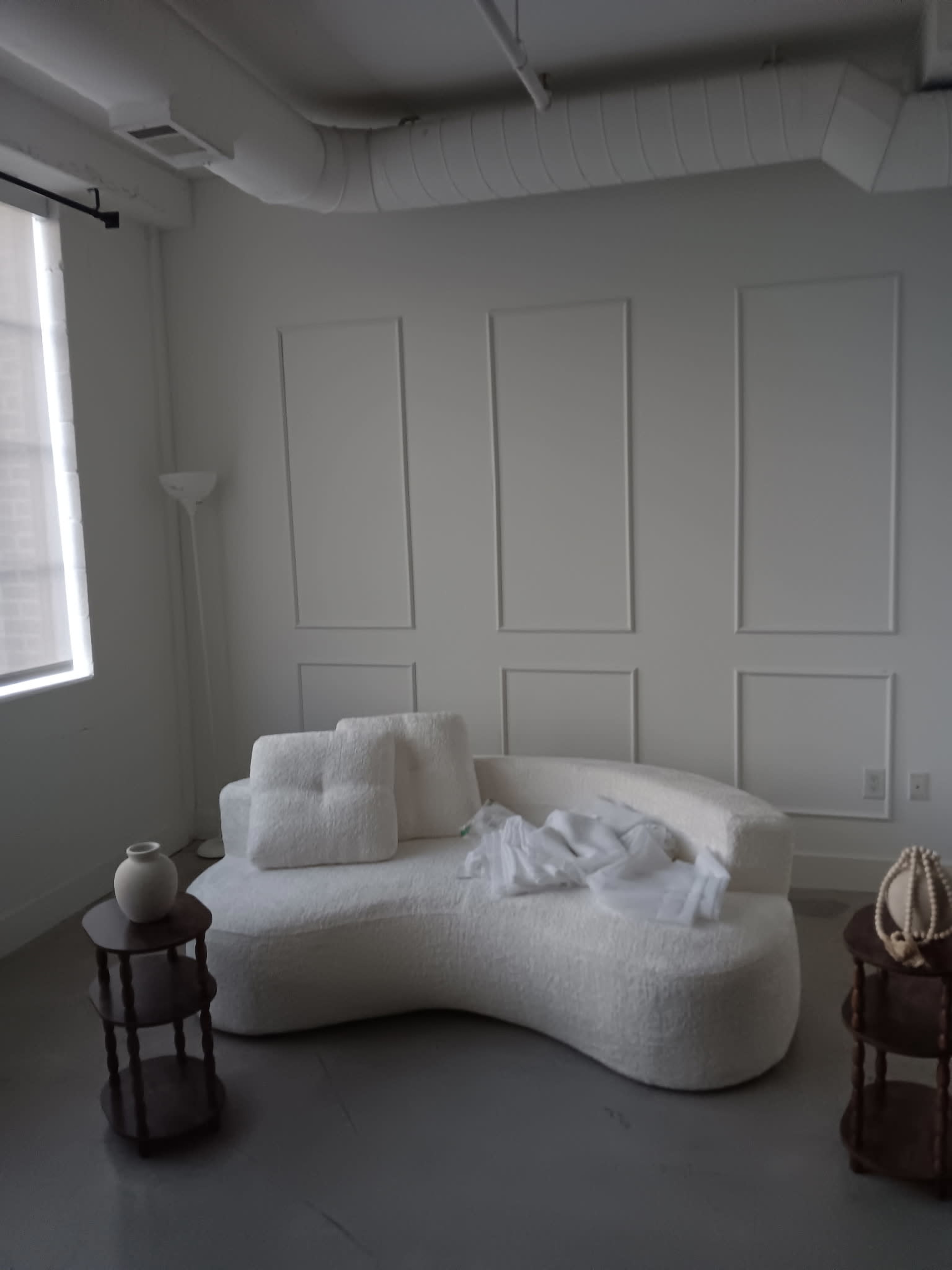 The image shows a minimalist room with a white curved couch, a small wooden side table, and a few decorative items on the table.