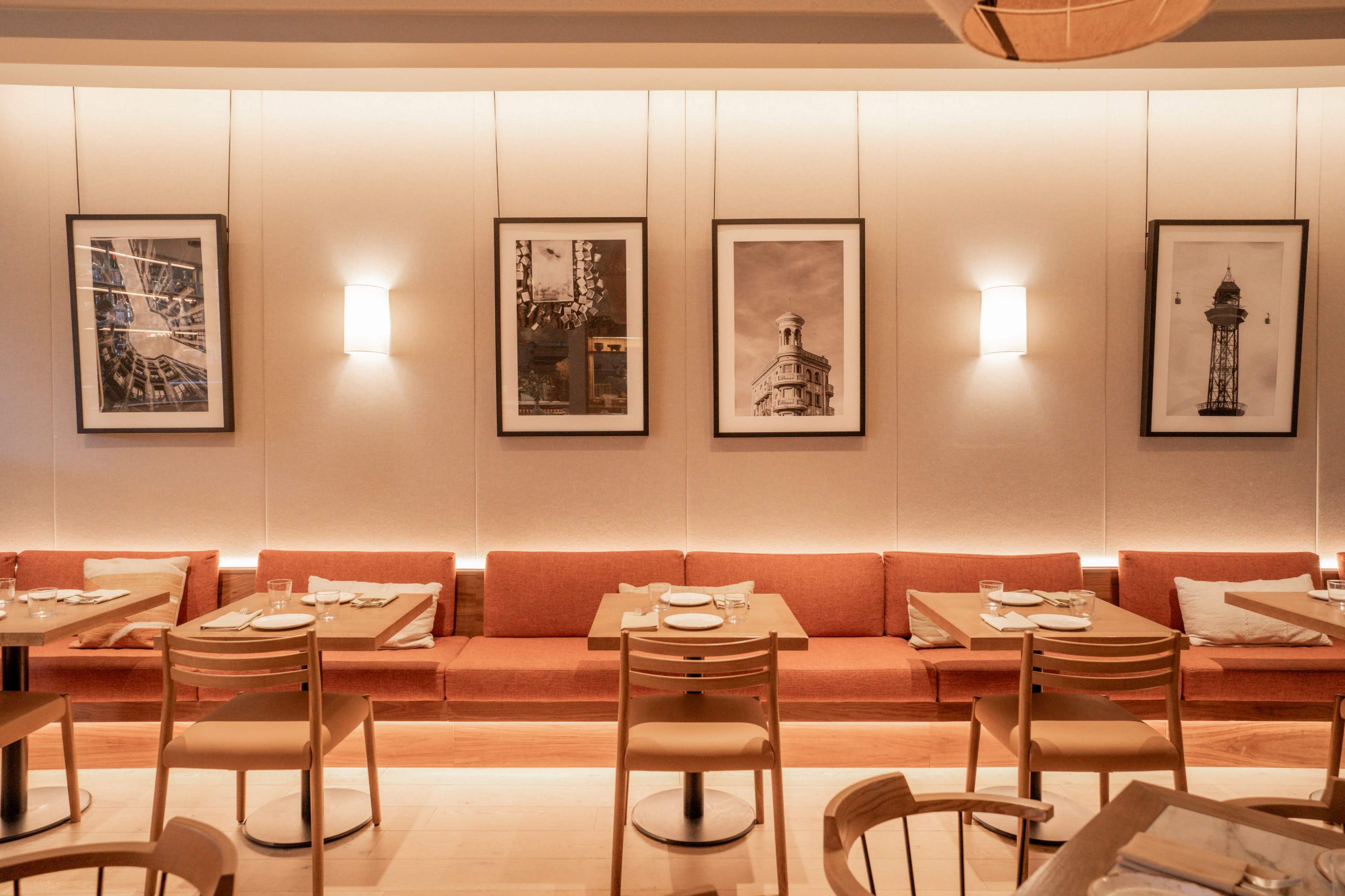 The image shows a restaurant interior with a series of framed black-and-white photographs on the walls, wooden tables, and orange seating along one side.