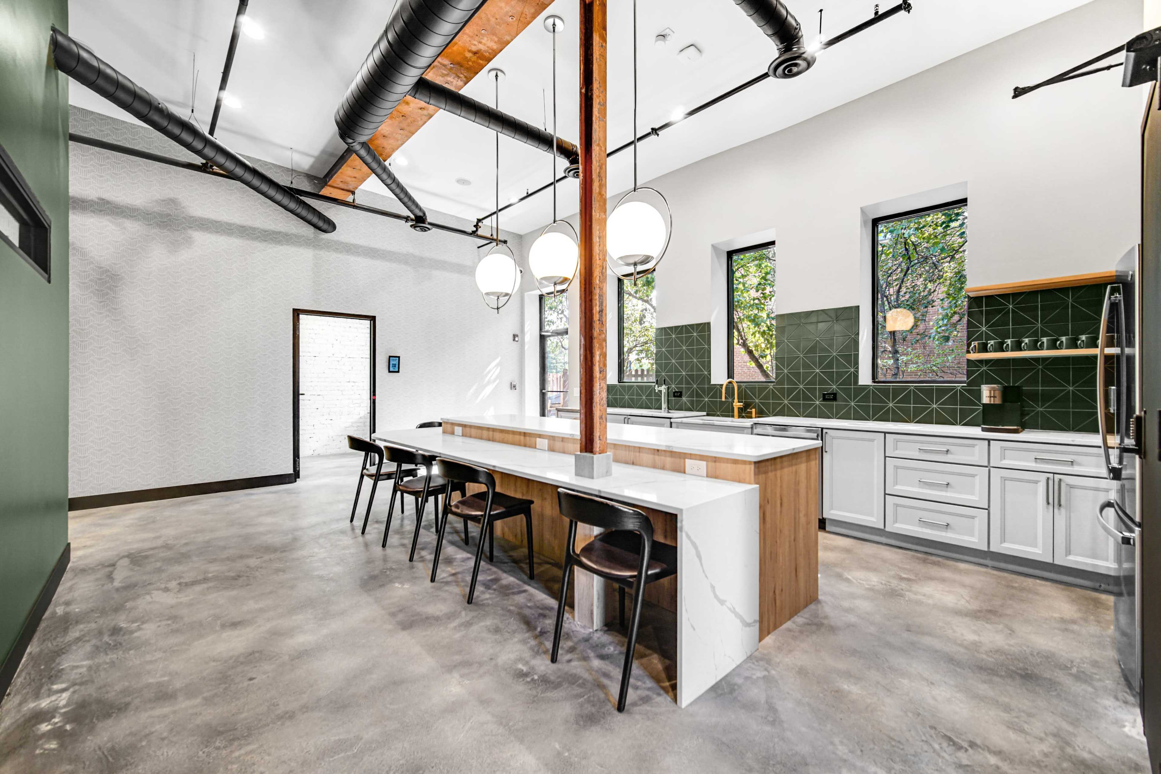A modern kitchen with a central island, sleek cabinets, and large windows allowing natural light to enter.