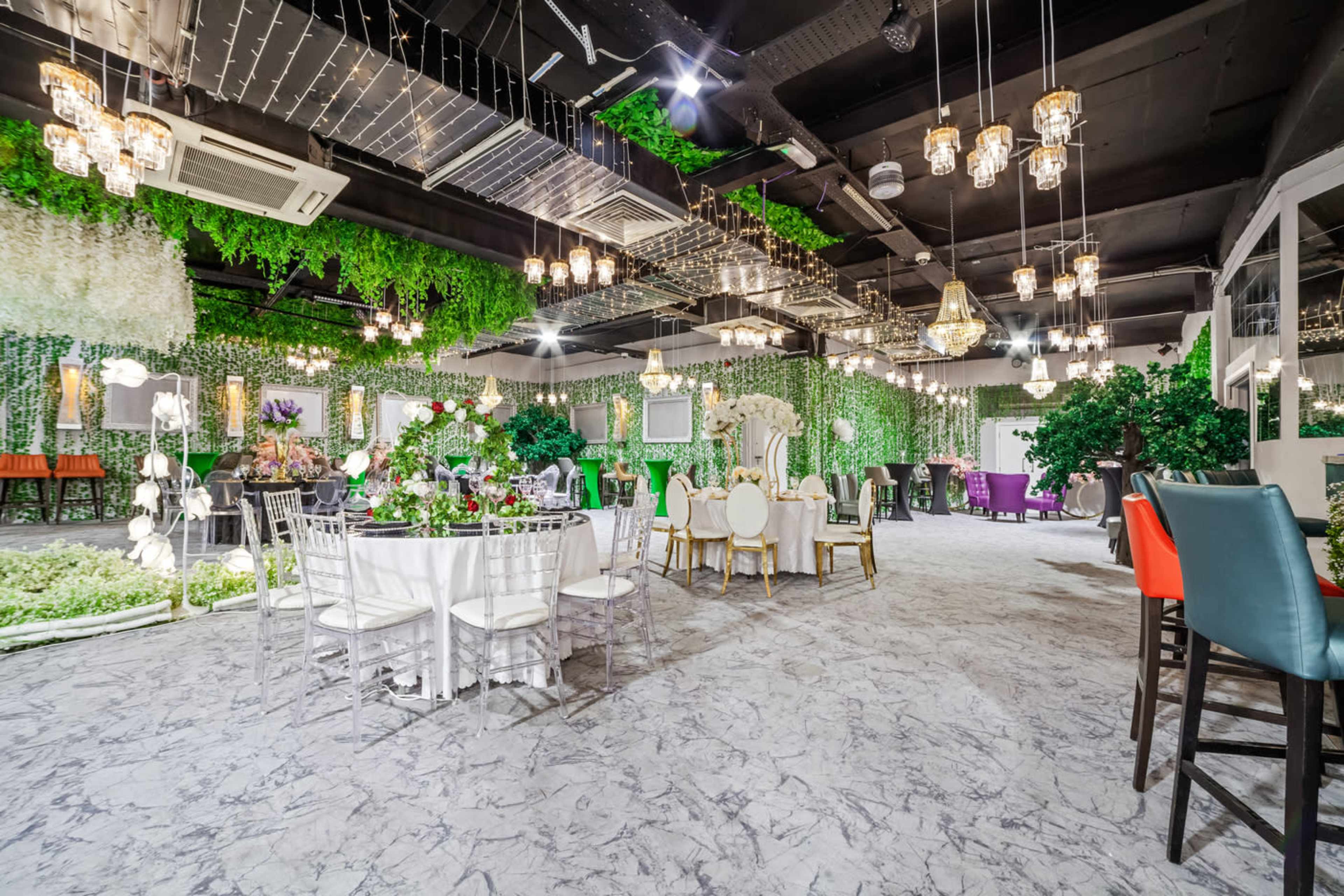 An elegantly decorated event space with tables set for dining, surrounded by lush greenery and hanging light fixtures.