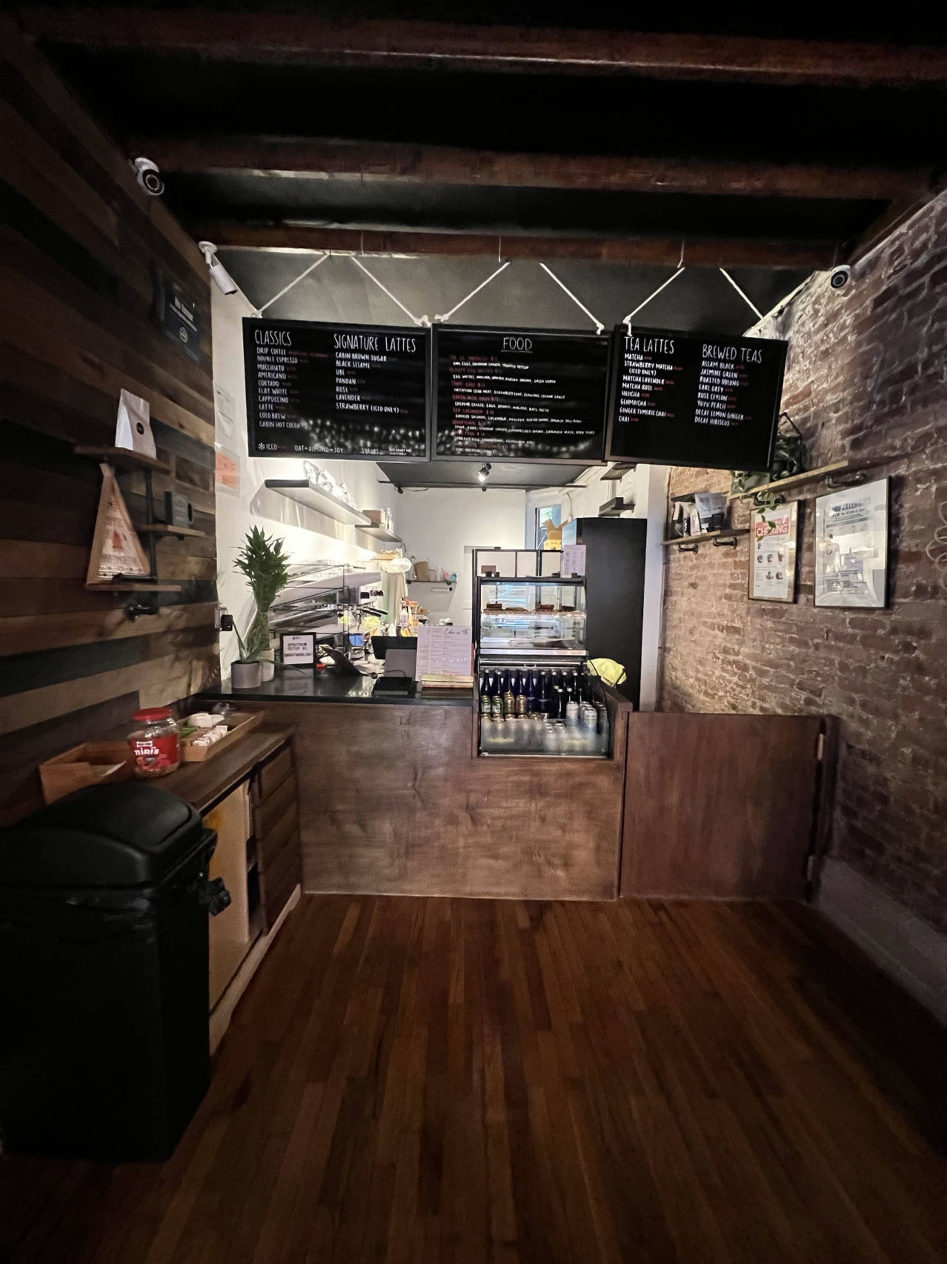 A rustic café interior with a wooden counter, a menu hanging above, and a visible food preparation area in the background.