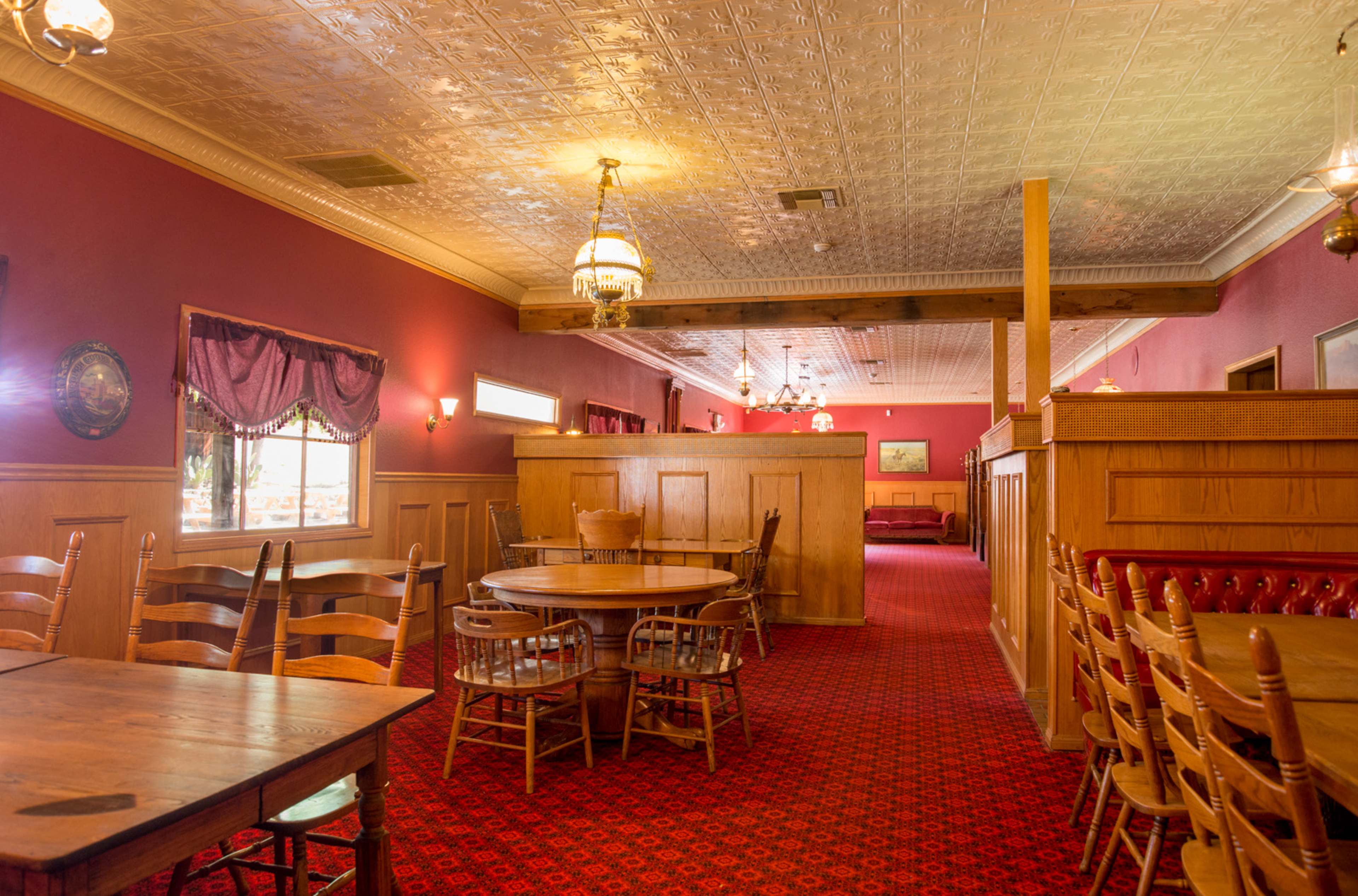 A spacious restaurant interior featuring wooden tables and chairs, red carpeting, and decorative wall panels.