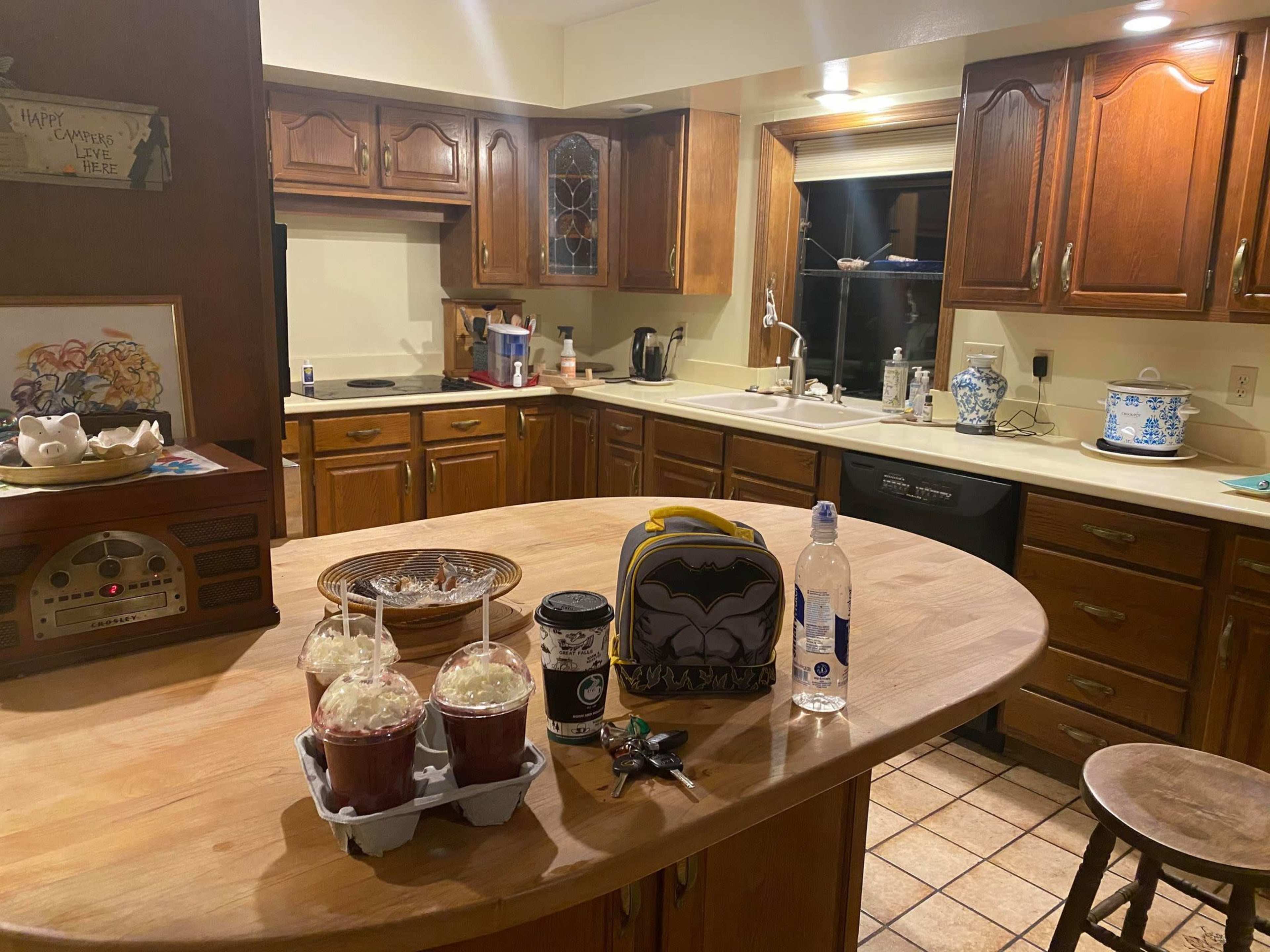 The kitchen features wooden cabinets, a large island with two drinks topped with whipped cream, a backpack, a water bottle, and a coffee cup on the counter.