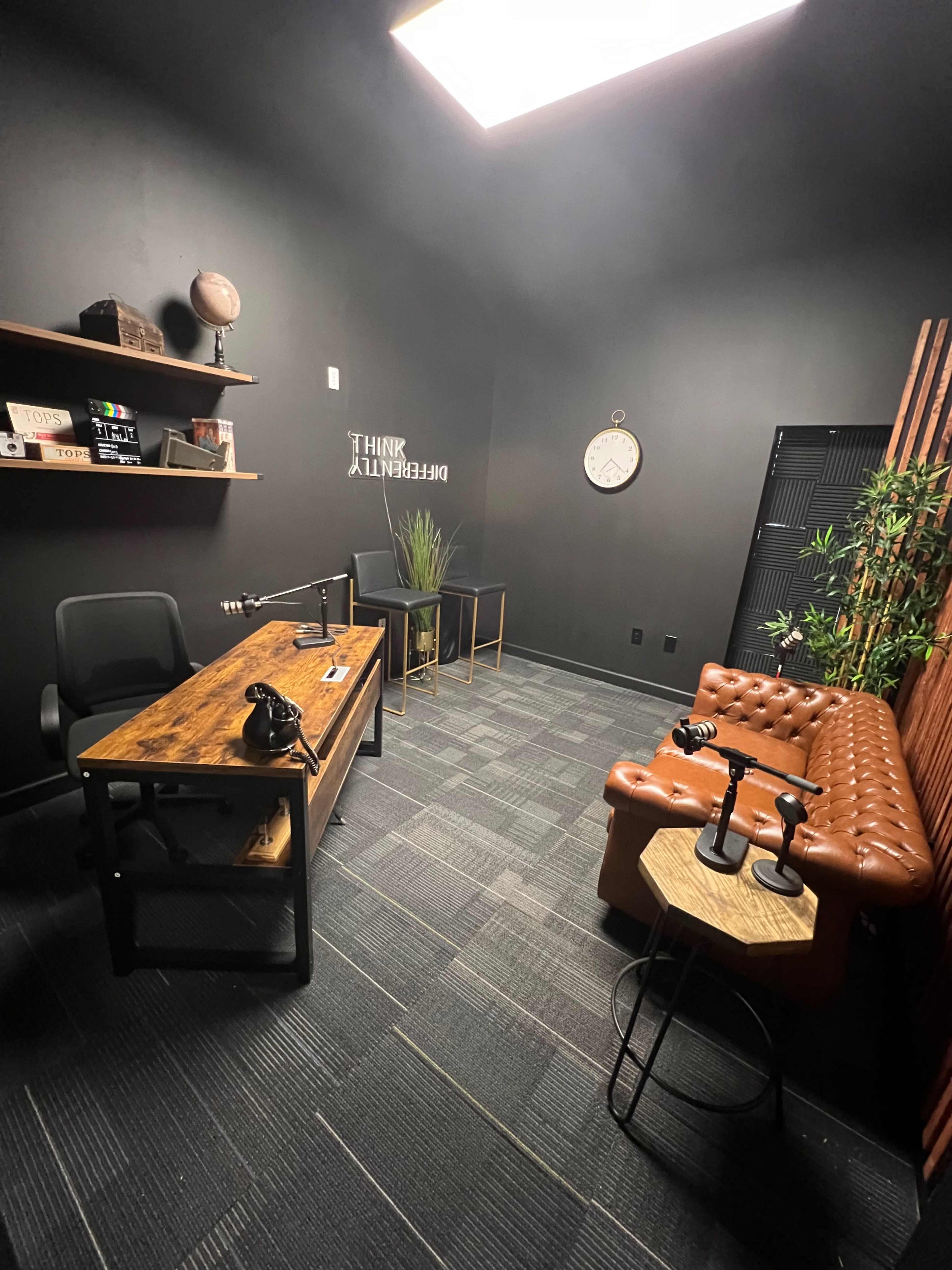 A modern office space featuring a wooden desk, a leather couch, and decorative shelves with various items.