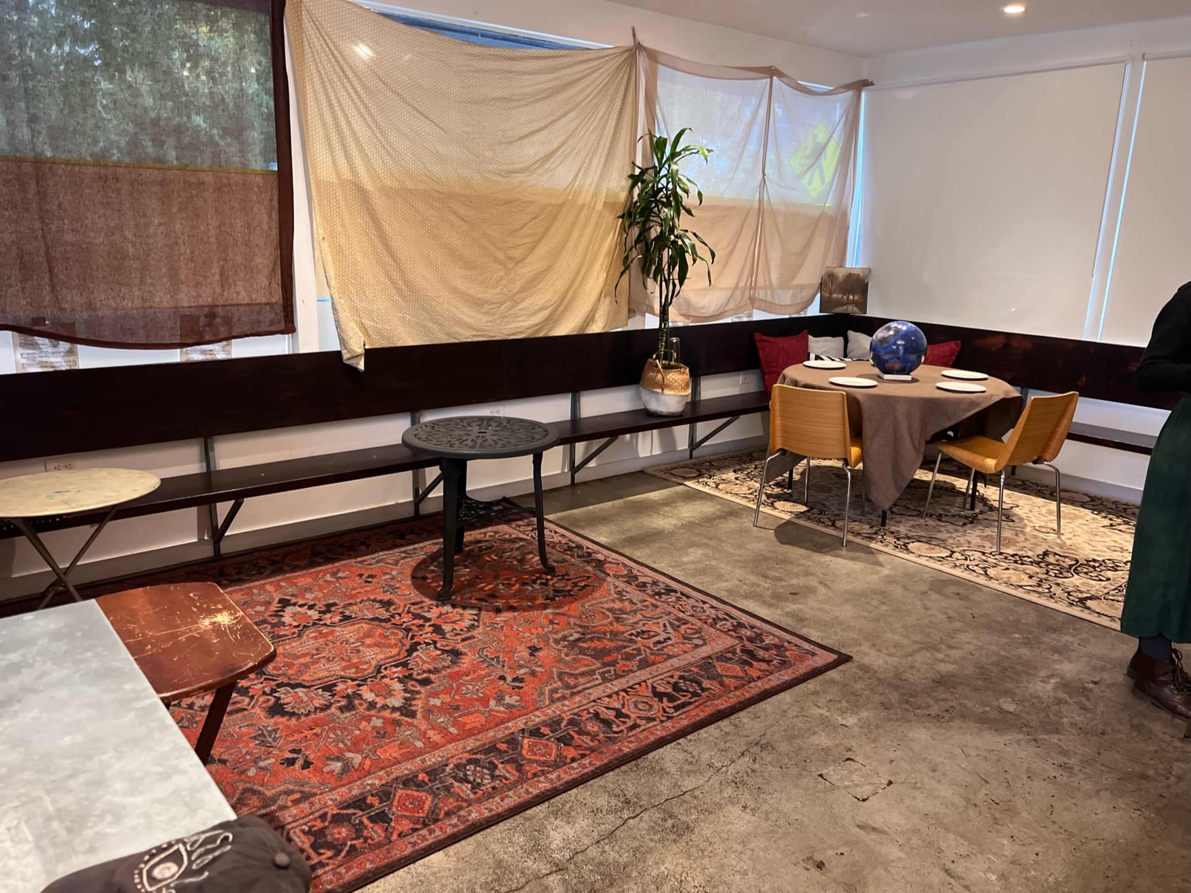 The image shows a casual dining space with tables and chairs, featuring an area rug and draped fabric on the walls for decoration.