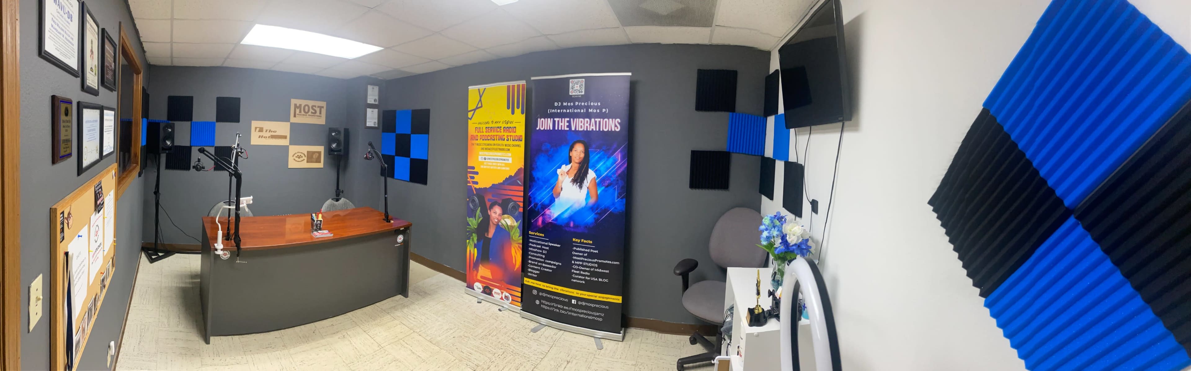 A recording studio with a desk, banners, and acoustic foam panels on the walls.