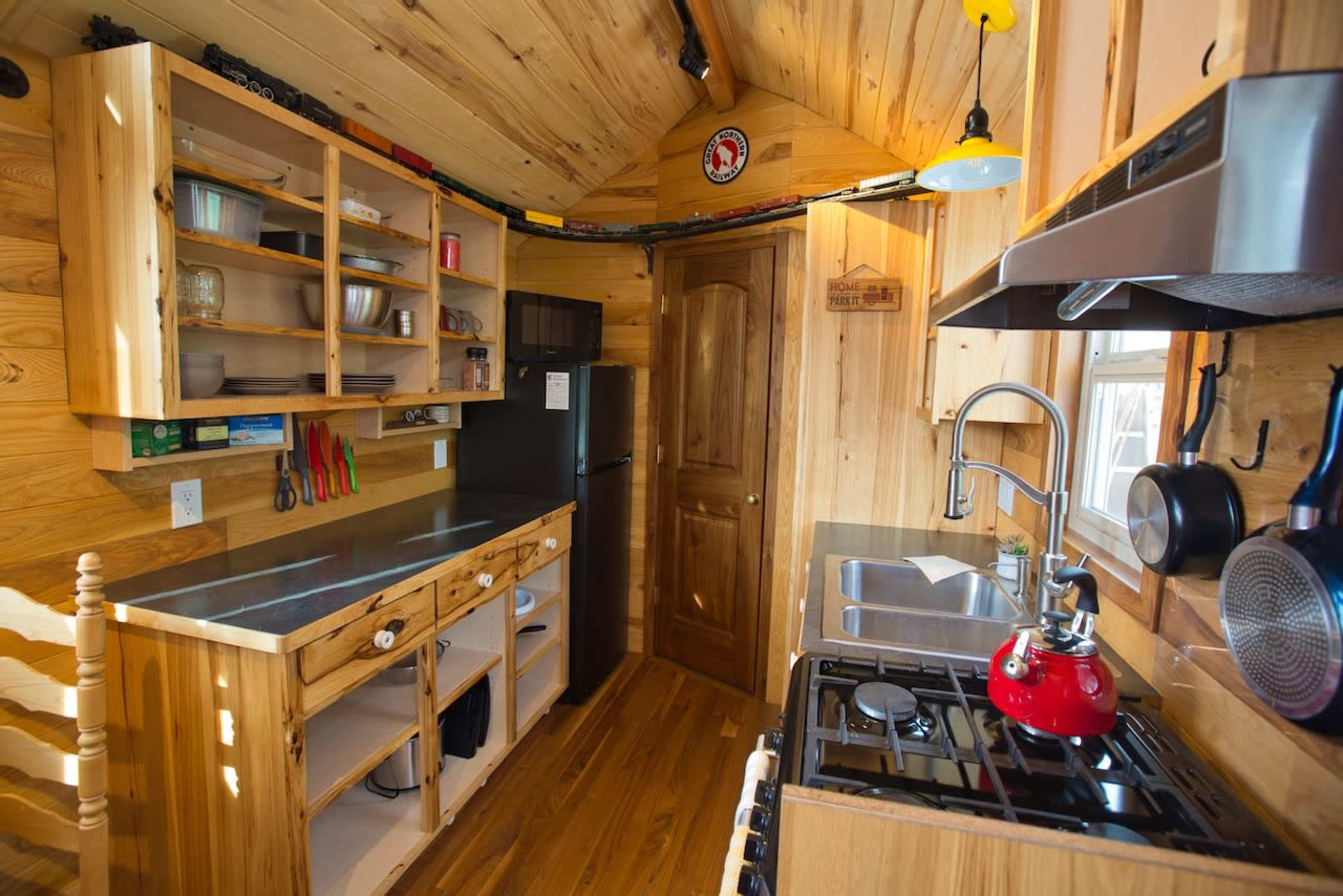 A small, well-organized kitchen with wooden cabinets, a stainless-steel sink, a gas stove, and a refrigerator.