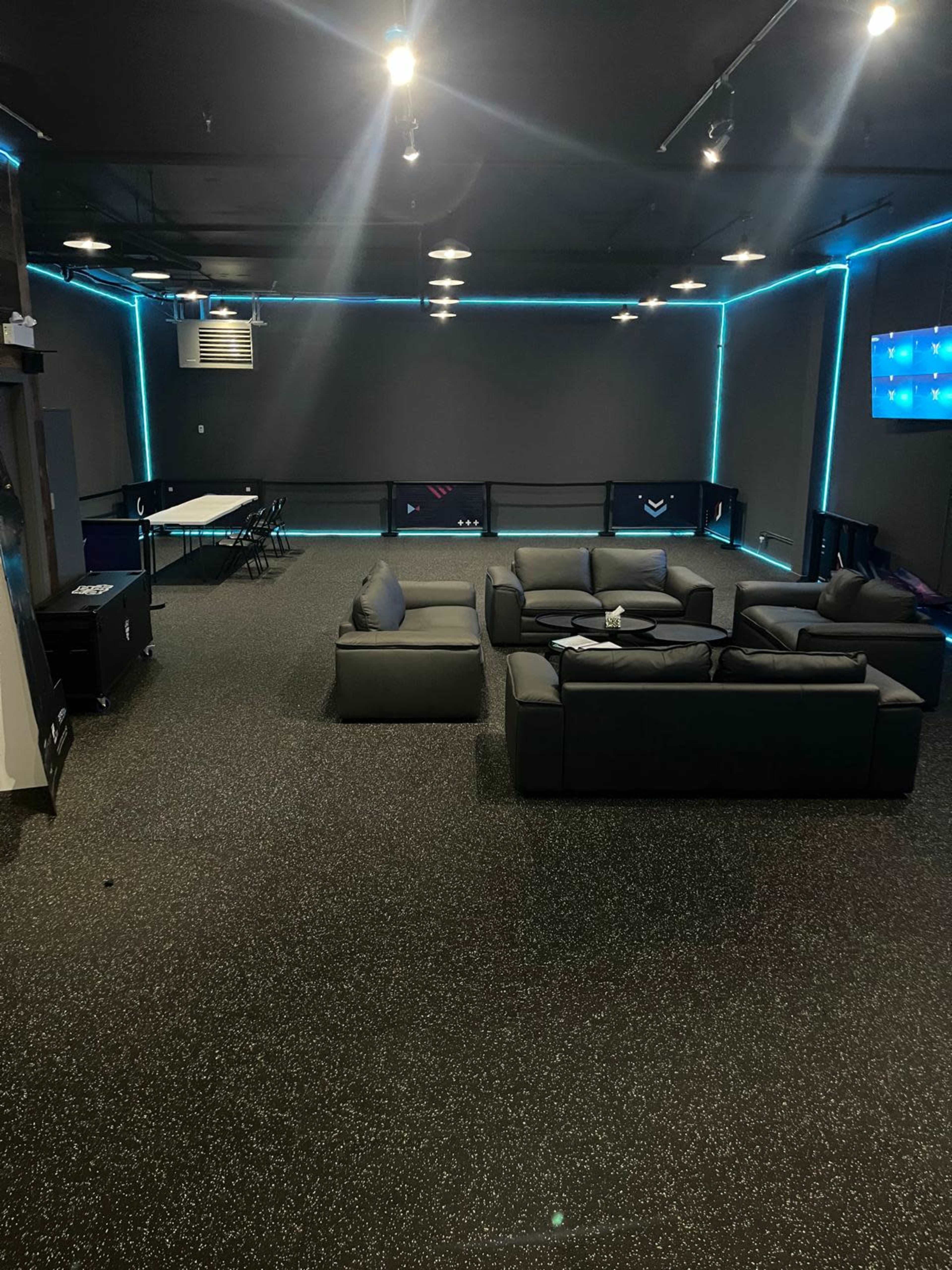 The image shows a modern lounge area with black furniture, a ping pong table, and blue LED lighting along the walls.
