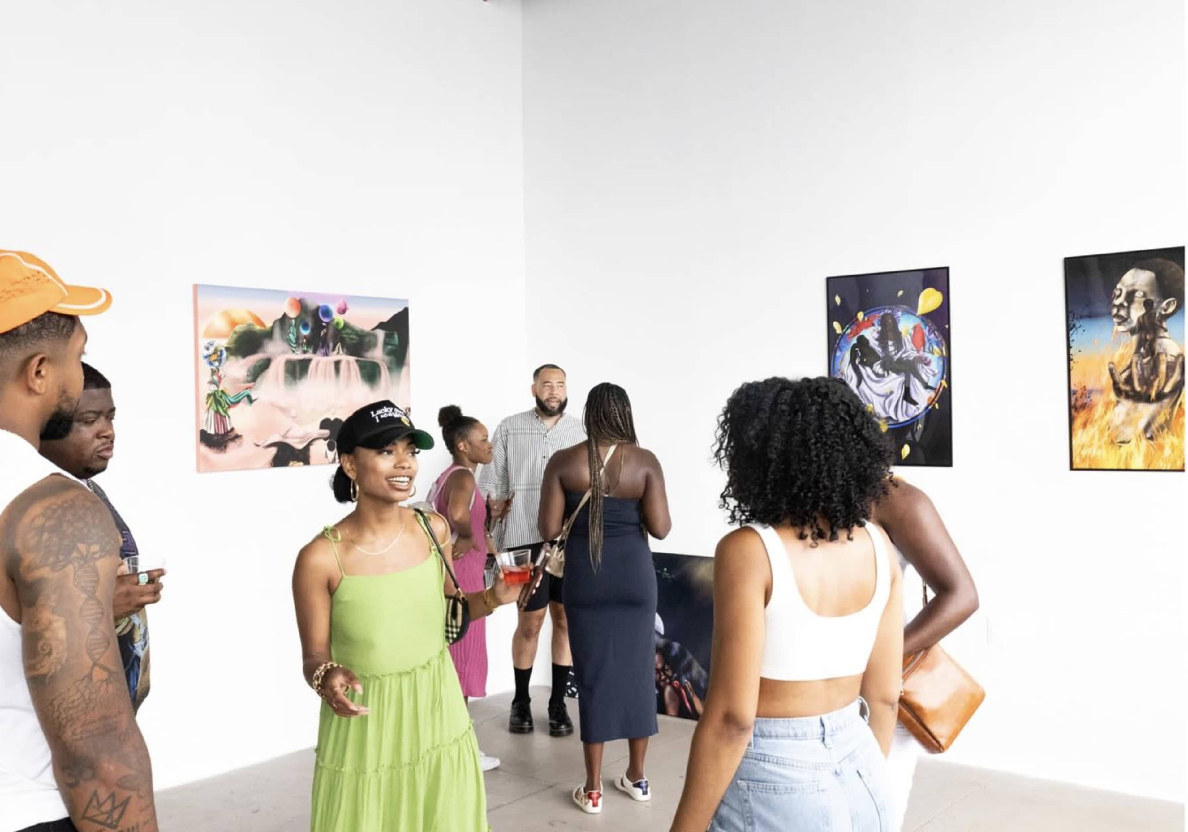 A group of people interacts in a gallery featuring colorful artworks on the walls.
