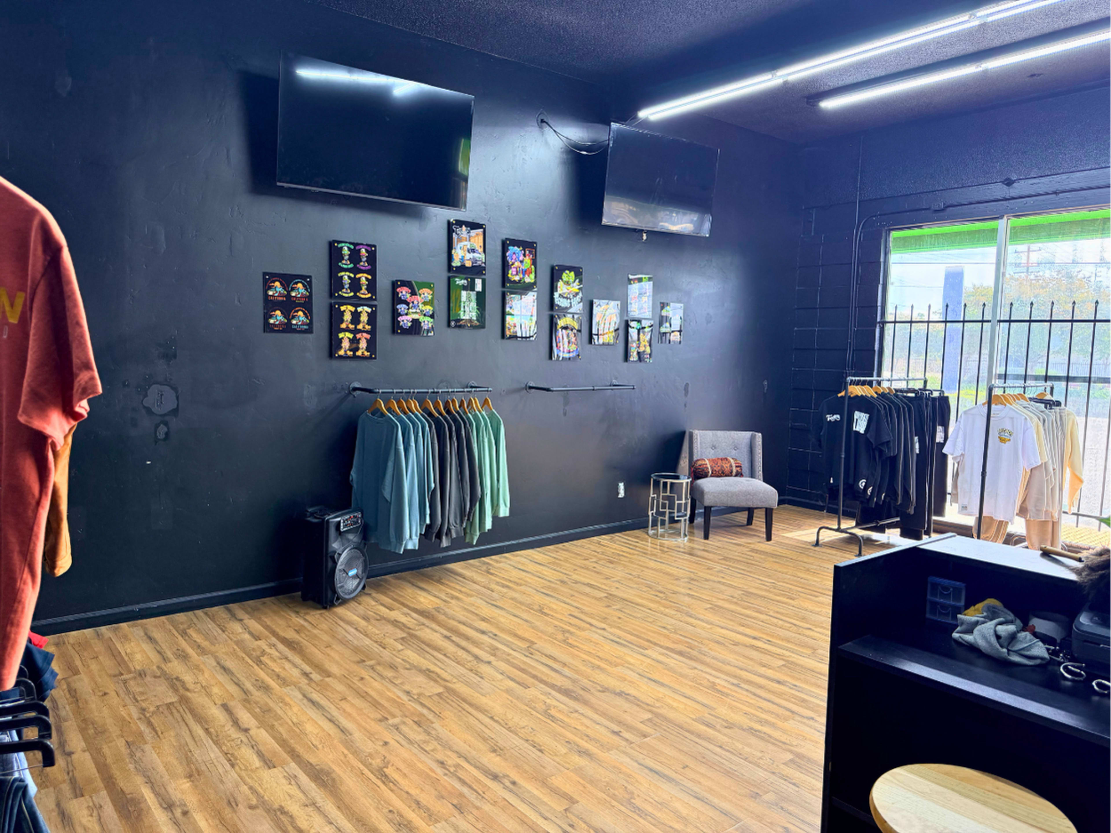 The image shows a clothing store with black walls, displaying a few racks of apparel and two televisions mounted on the wall.