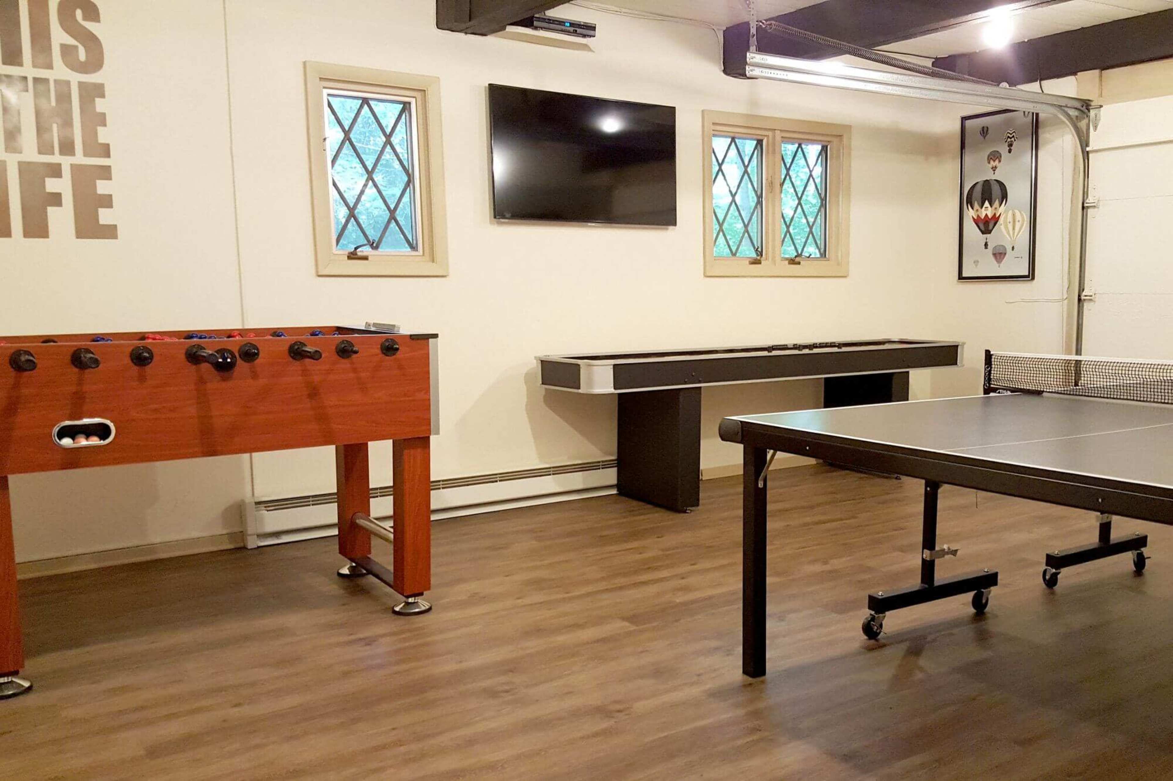 The image shows a recreational room with a foosball table, a ping pong table, and a wall-mounted television.