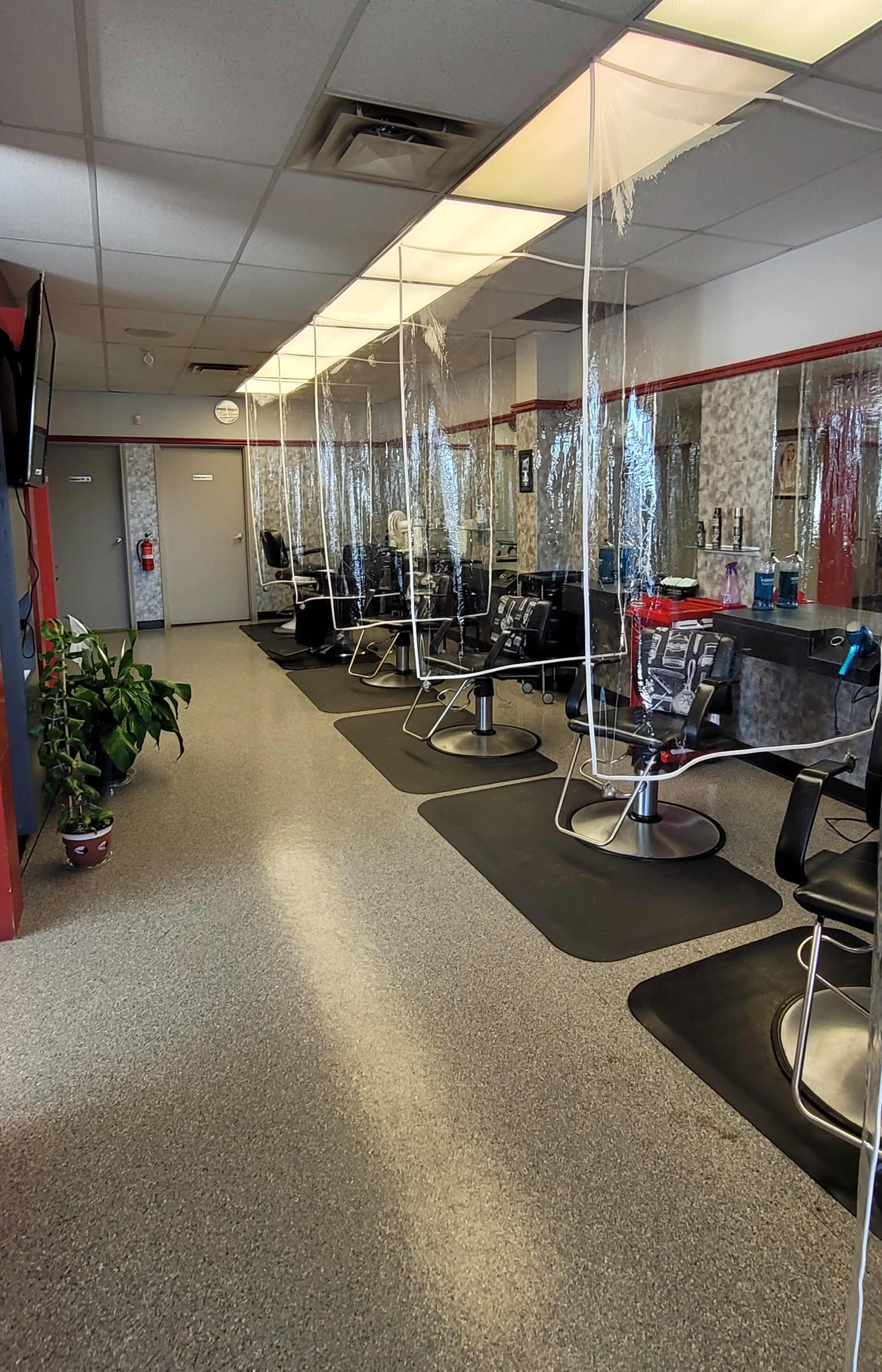 A hair salon interior with multiple styling stations separated by sheer plastic dividers.