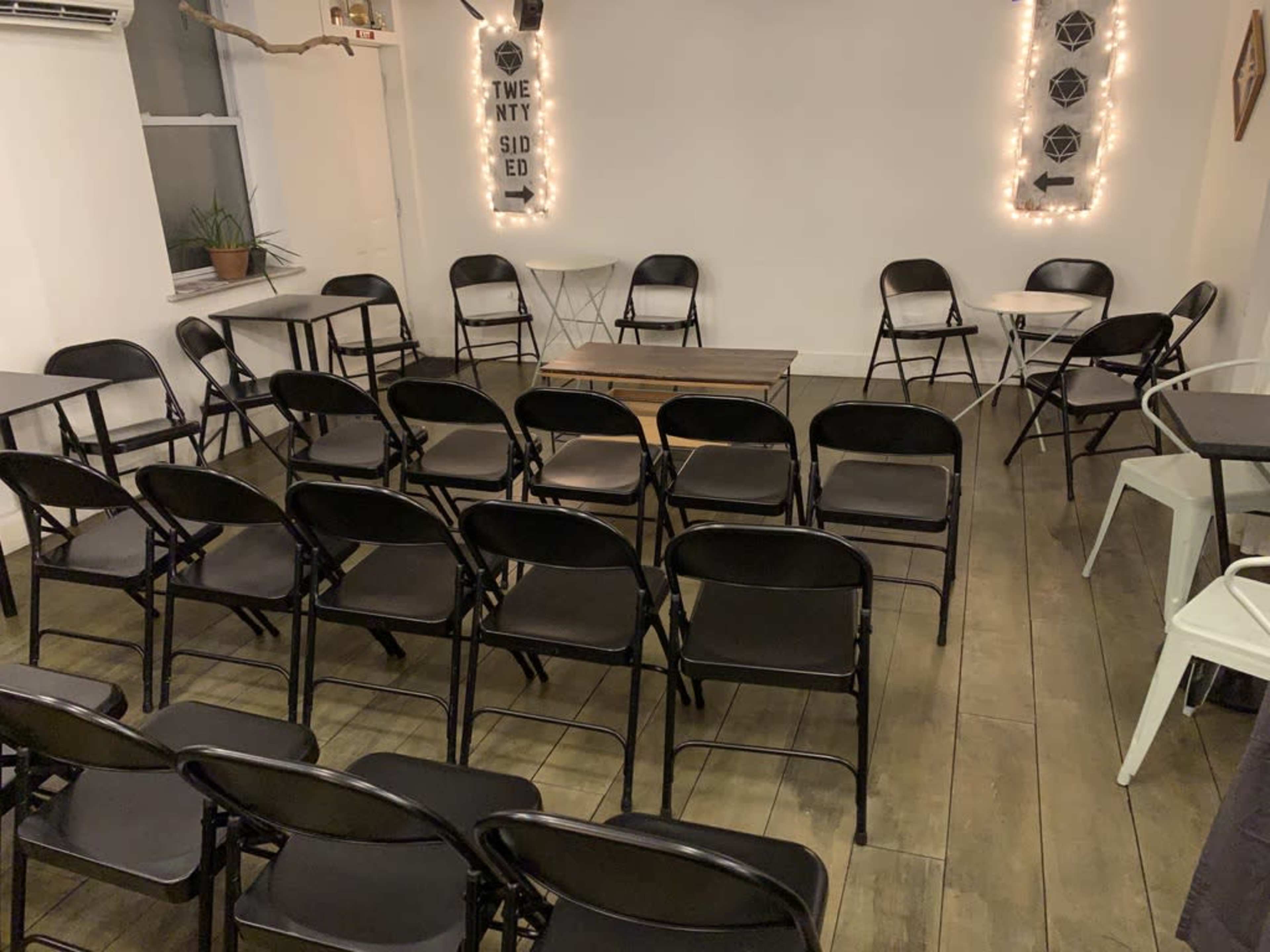 A room with black folding chairs arranged in rows facing a central table, surrounded by white walls and soft lighting.