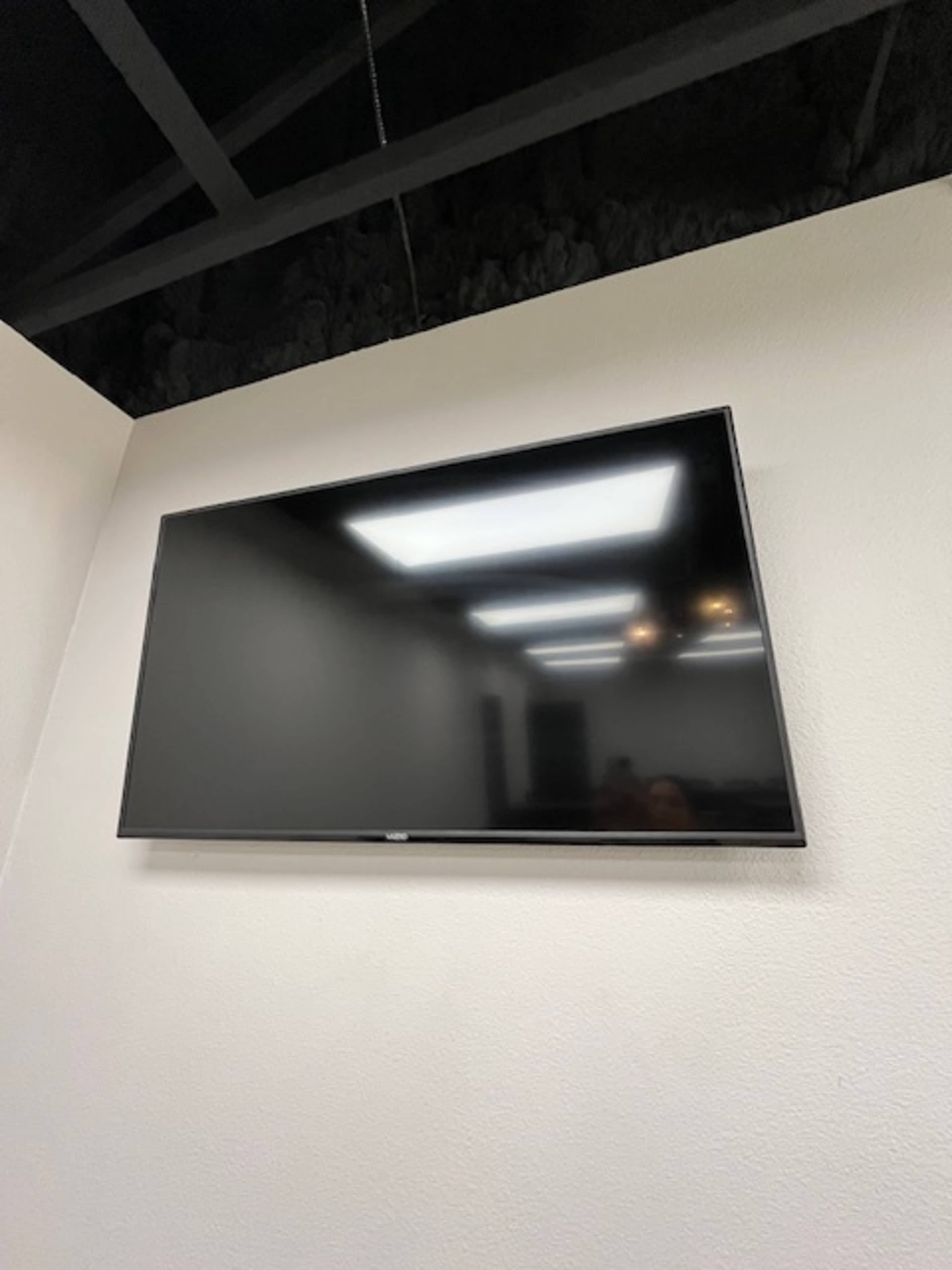 A flat-screen television is mounted on a white wall in a room with a dark ceiling.