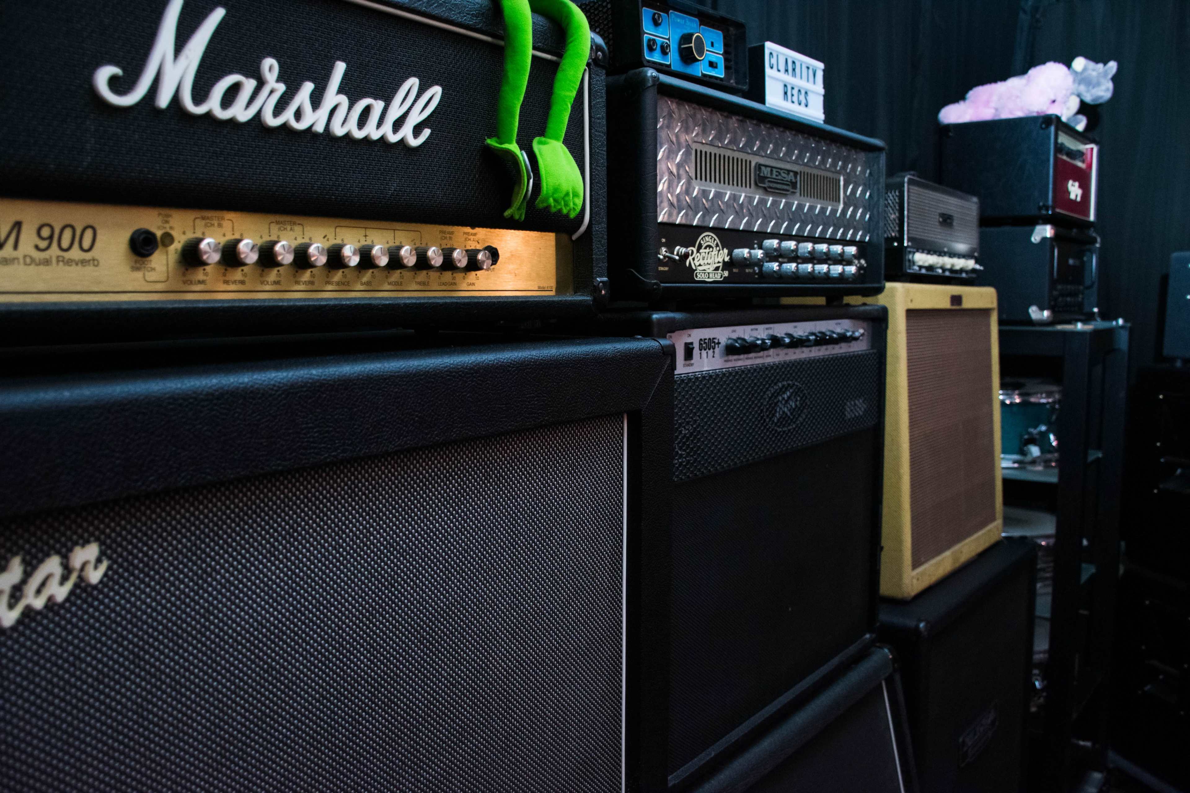 The image shows a collection of amplifiers and speaker cabinets lined up against a black backdrop.