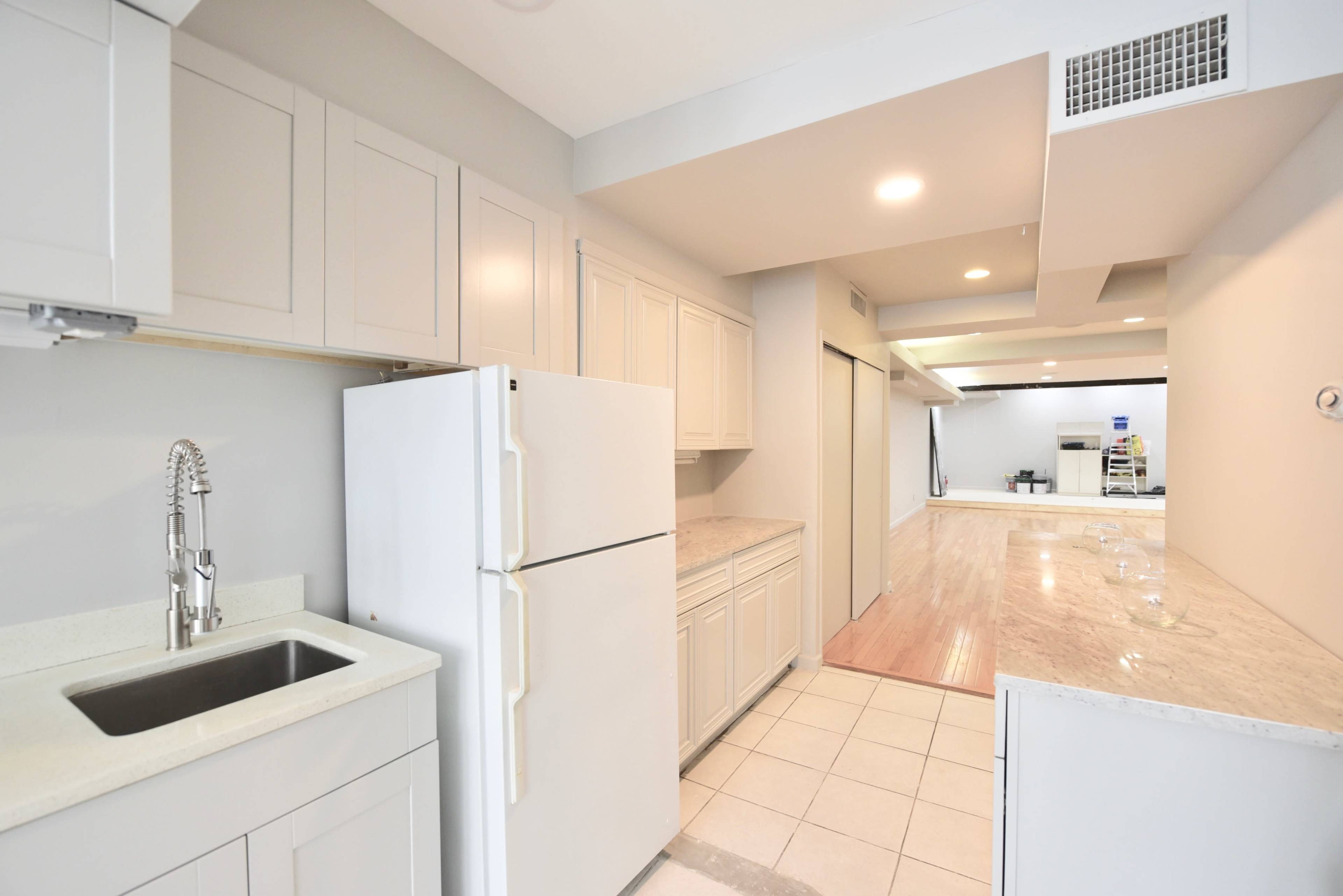 A modern kitchen features light cabinetry, a white refrigerator, and granite countertops, leading to an open space beyond.