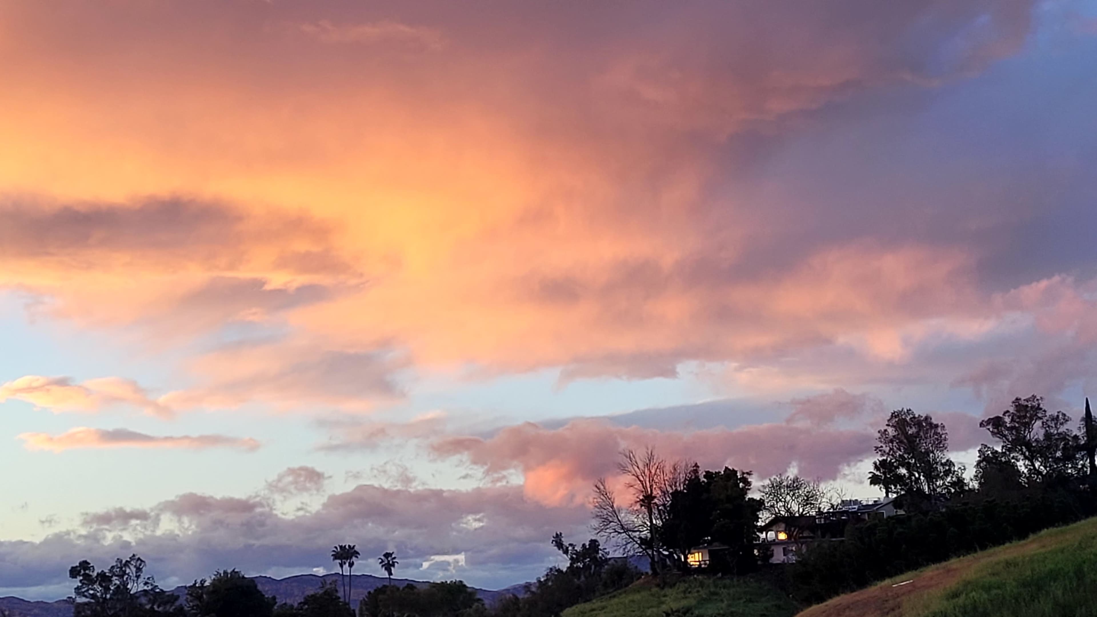The scene features a colorful sunset with pink and orange clouds above a landscape that includes trees and a house.