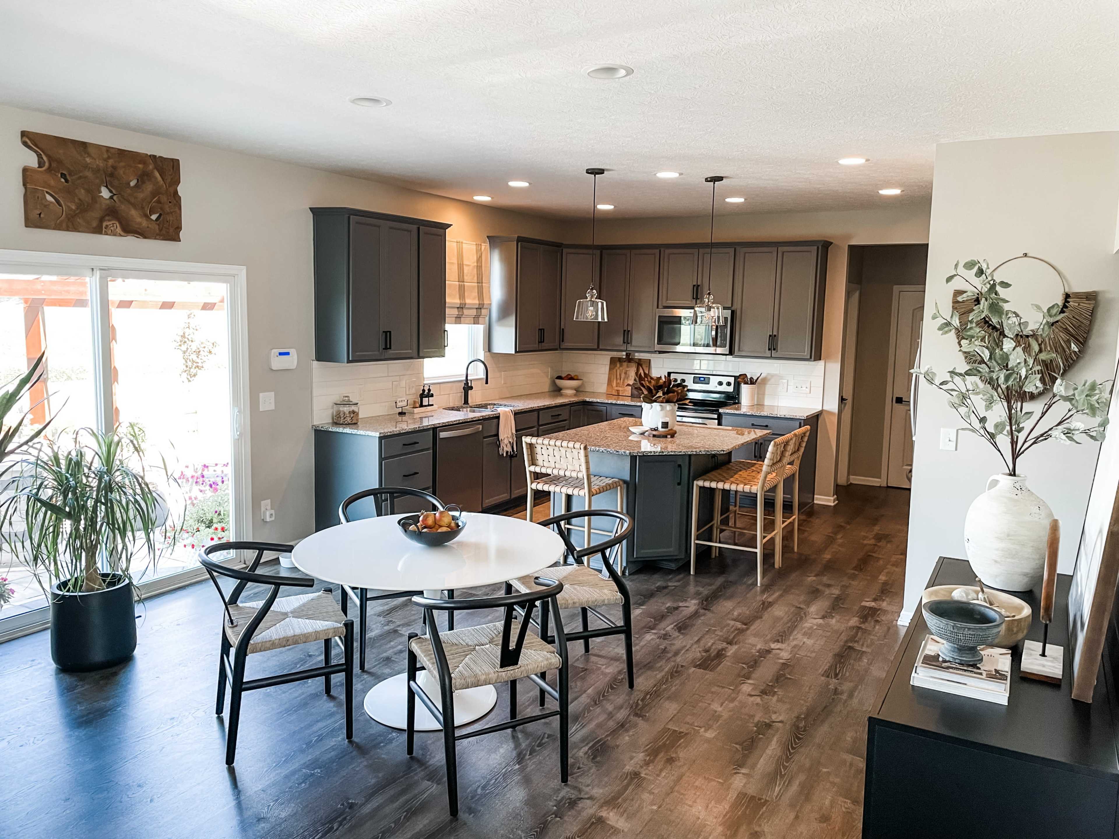 A modern kitchen and dining area feature gray cabinetry, a central island with bar seating, and a round dining table surrounded by chairs.