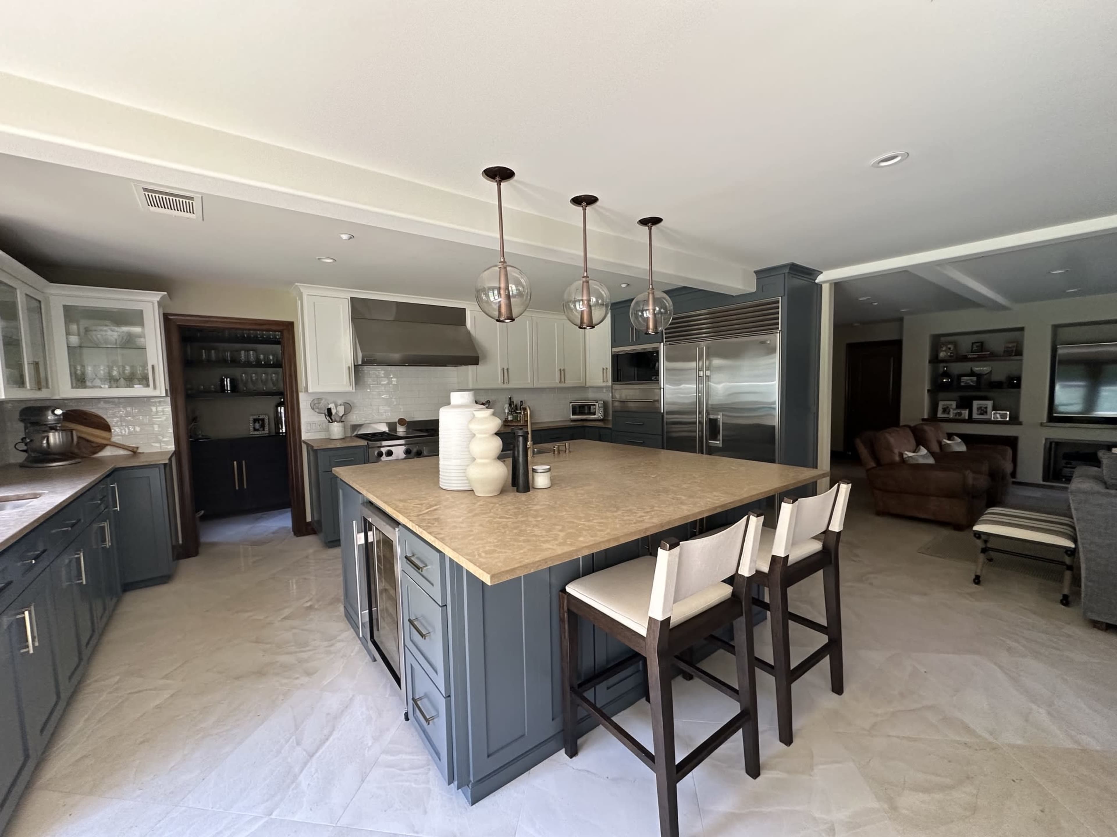 The image shows a modern kitchen featuring a large island with bar stools, stainless steel appliances, and light-colored cabinetry.