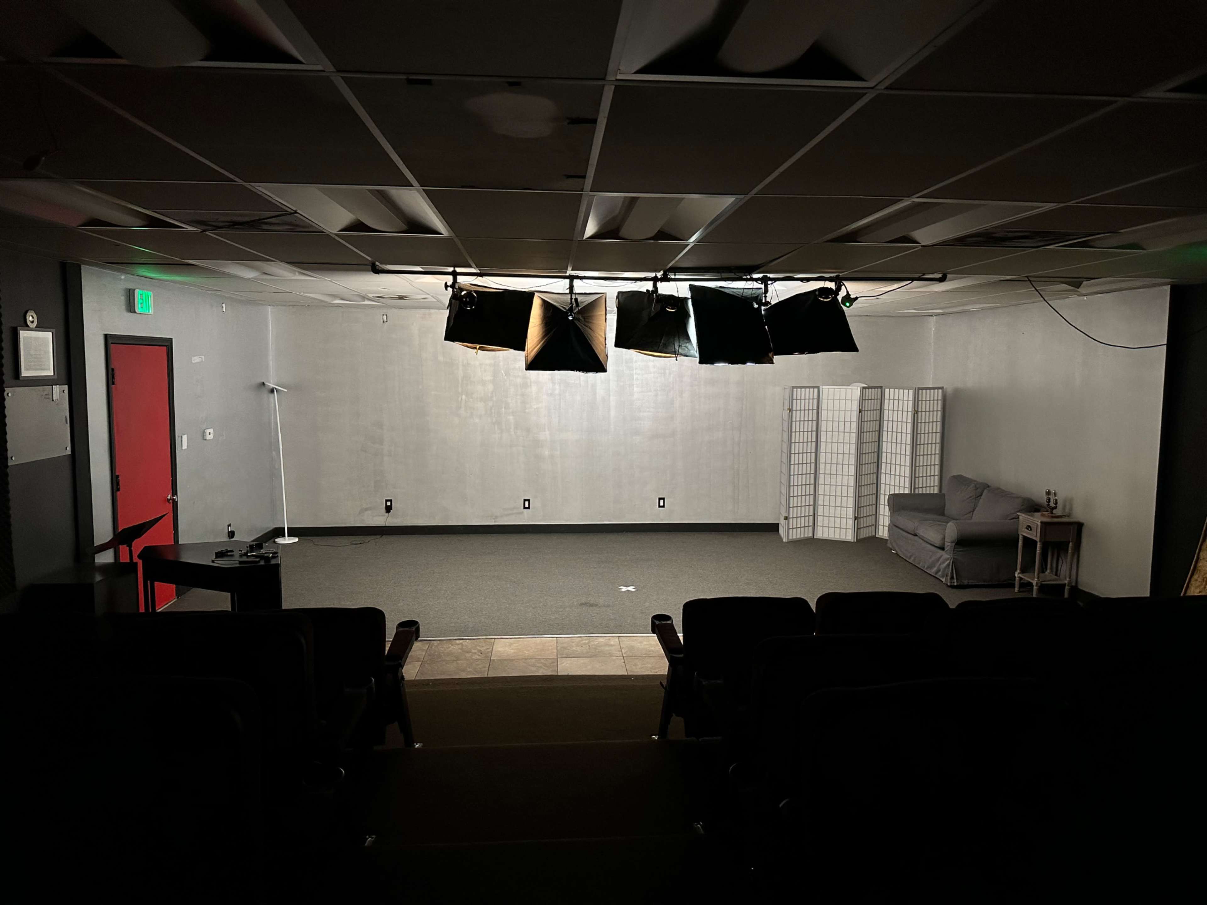 A dimly lit room with a row of chairs, a couch in the corner, and a lighting rig hanging from the ceiling.
