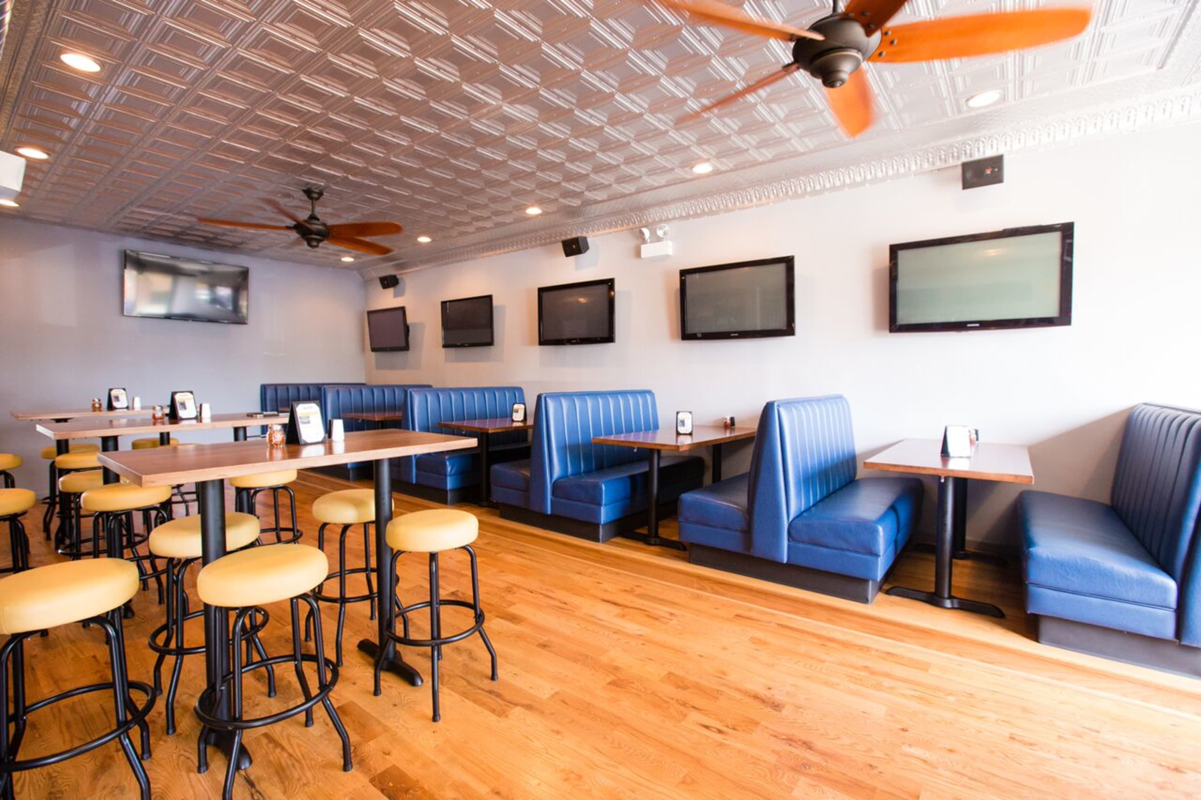 The image shows a restaurant interior with blue booth seating, wooden tables, and multiple flat-screen TVs mounted on the walls.
