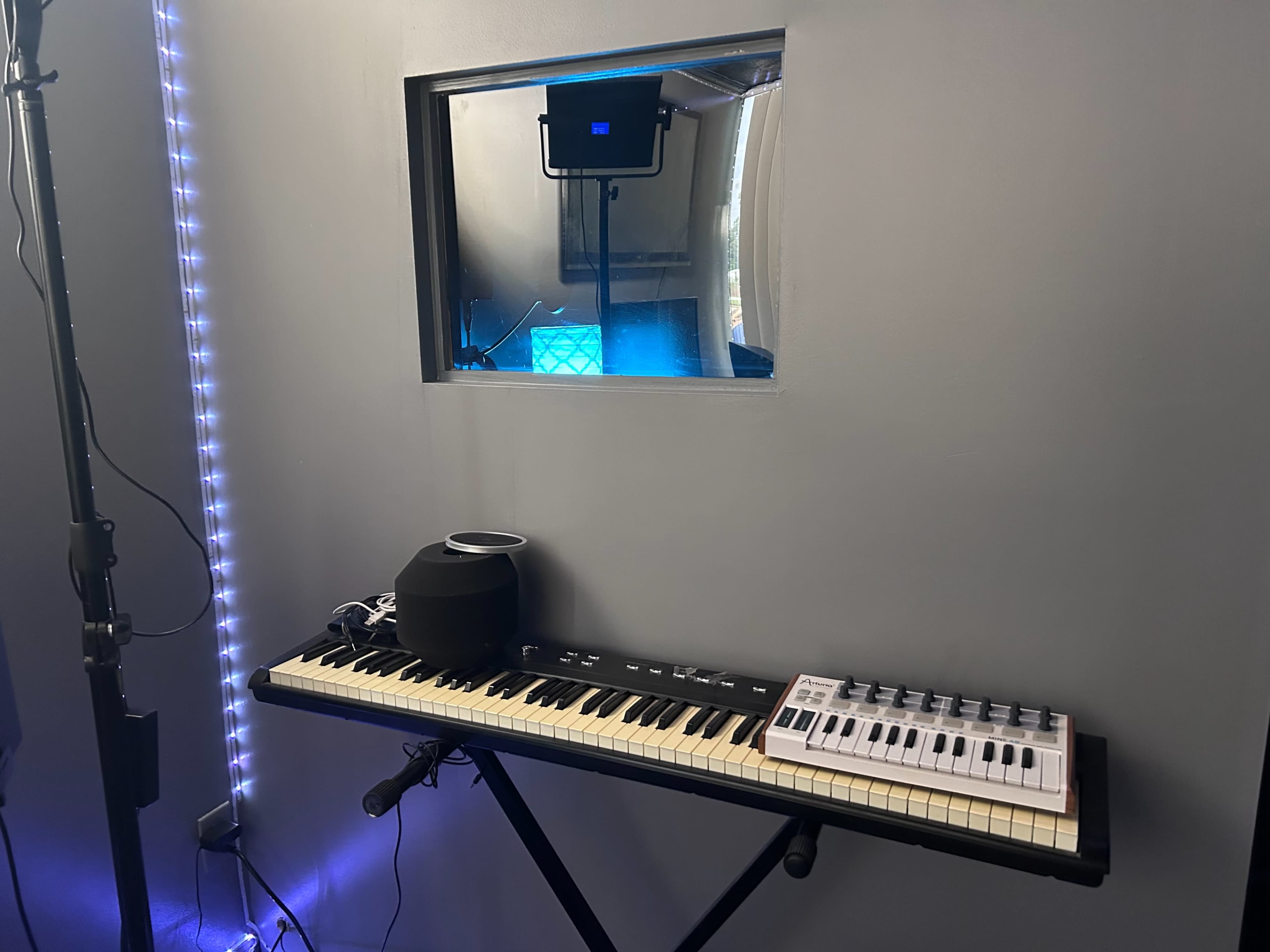 A keyboard and a small speaker are positioned in front of a window looking into a room illuminated with blue light.