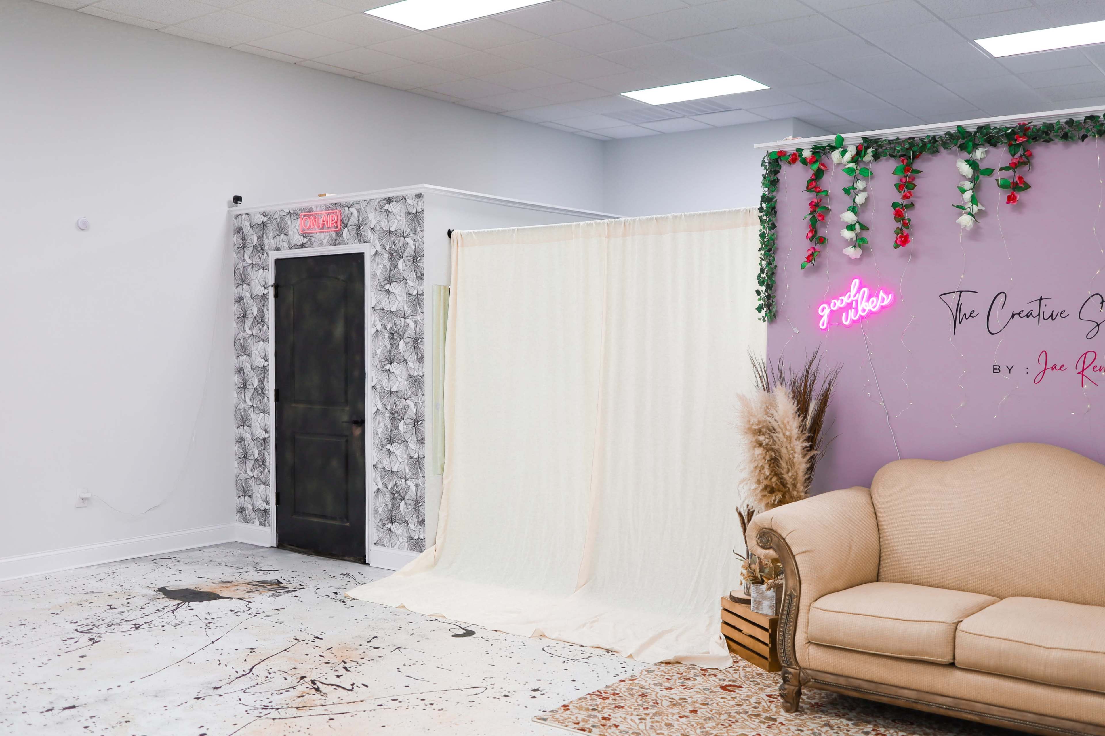 The image shows a spacious interior with a beige sofa, a textured backdrop, and a decorative wall featuring a neon sign and plants.