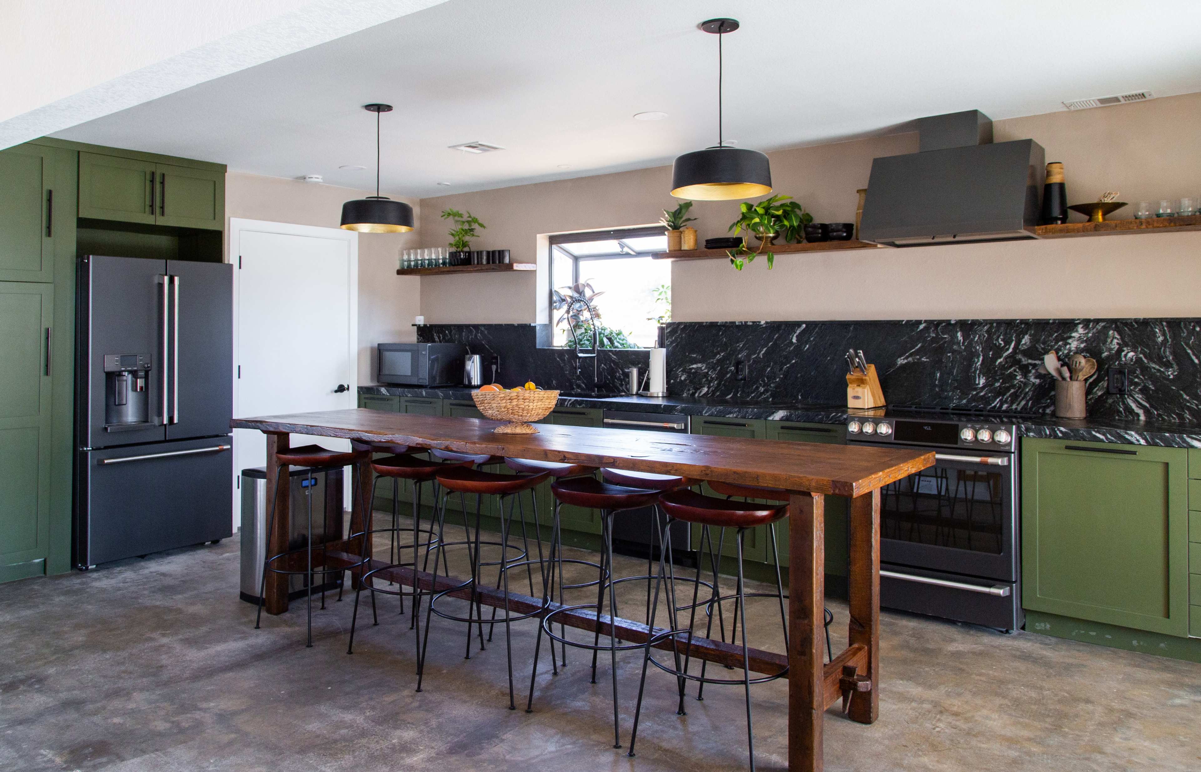 The kitchen features dark green cabinets, a large wooden island with bar seating, and a black stone backsplash with modern appliances.