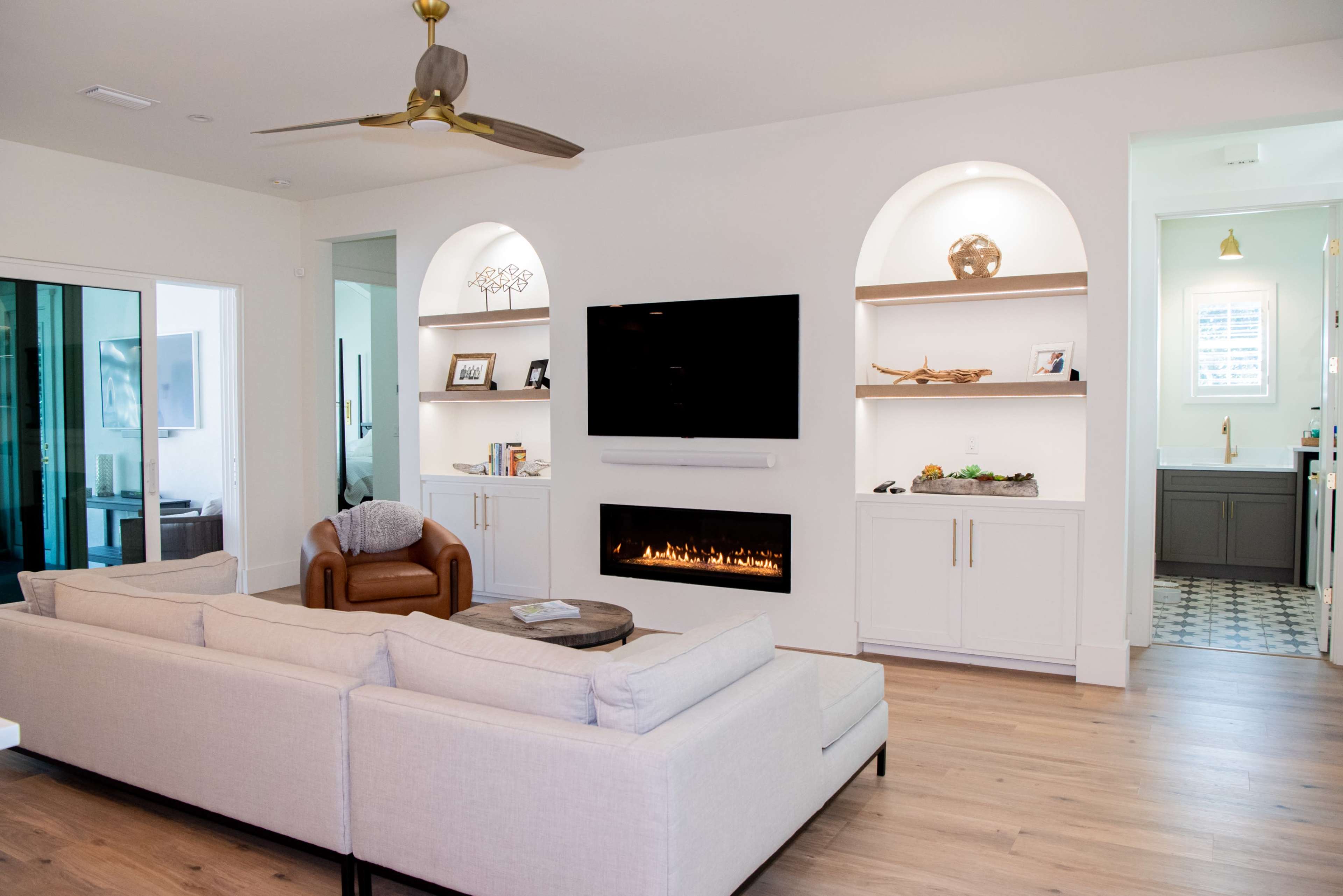 The image shows a modern living room with a sectional sofa, a wall-mounted television, built-in shelves, and an electric fireplace beneath the TV.