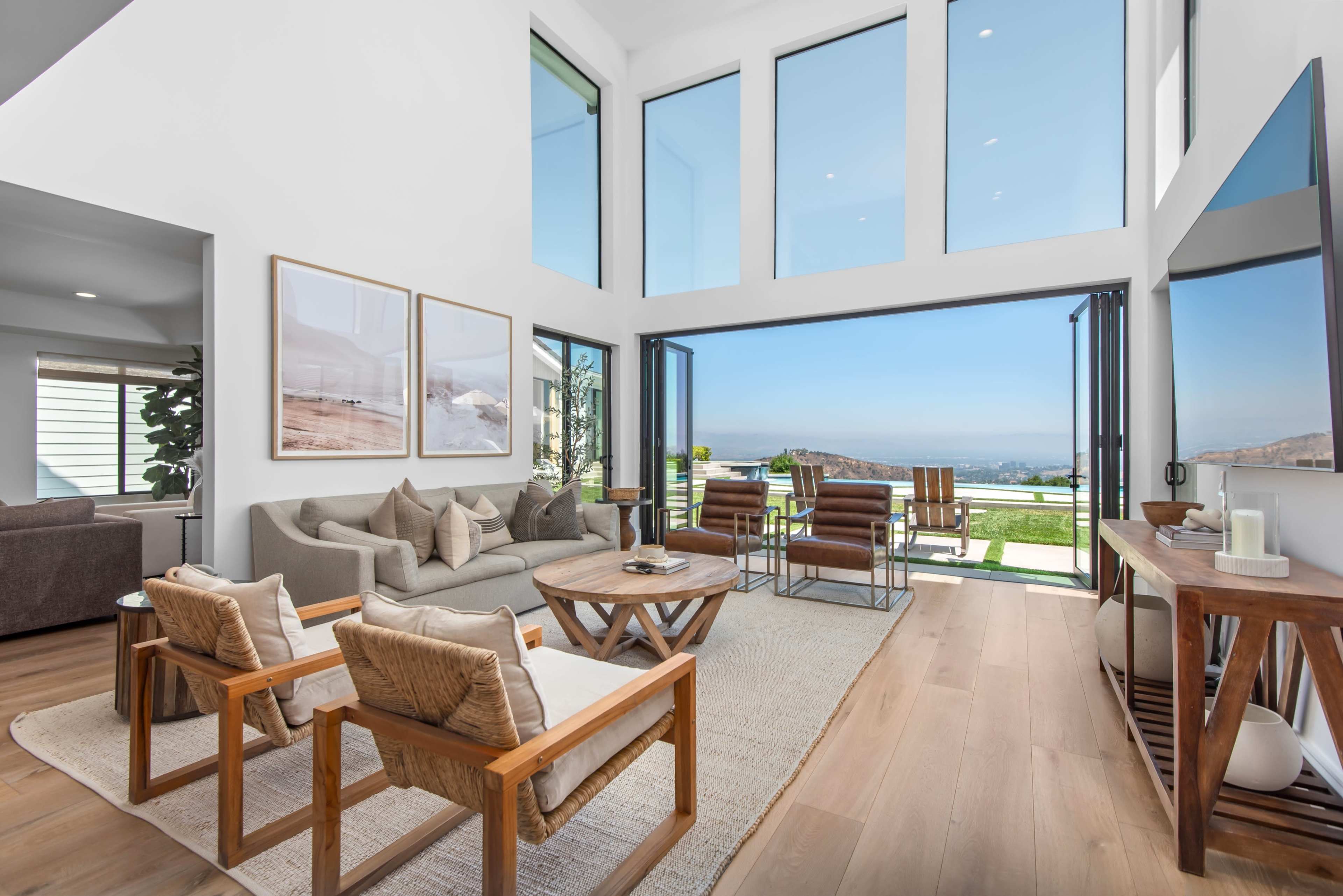 A modern living room features large windows, minimalist furniture, and opens to a patio with a view.