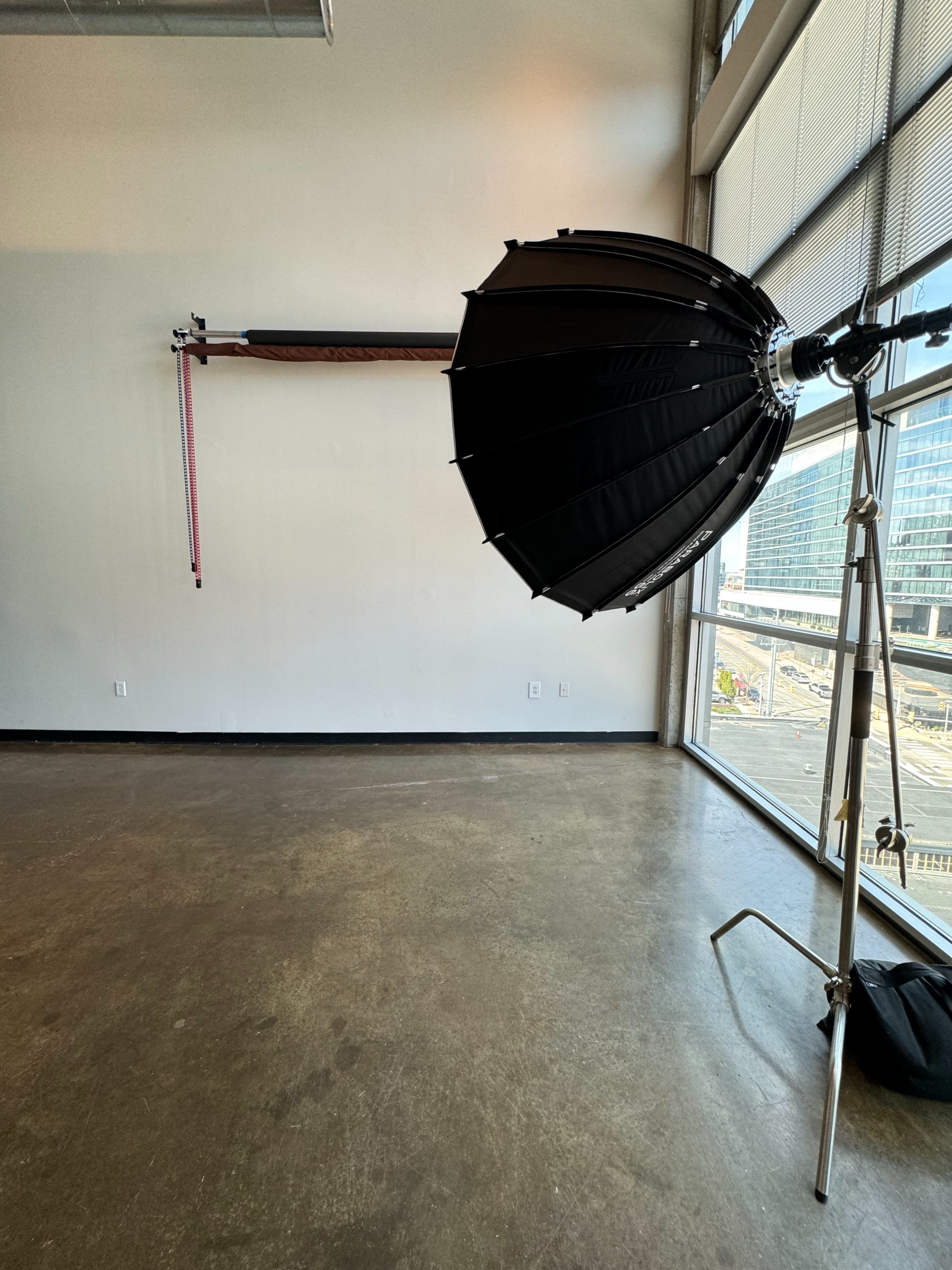 A photography studio with a large softbox light on a stand and a wall-mounted backdrop support system.
