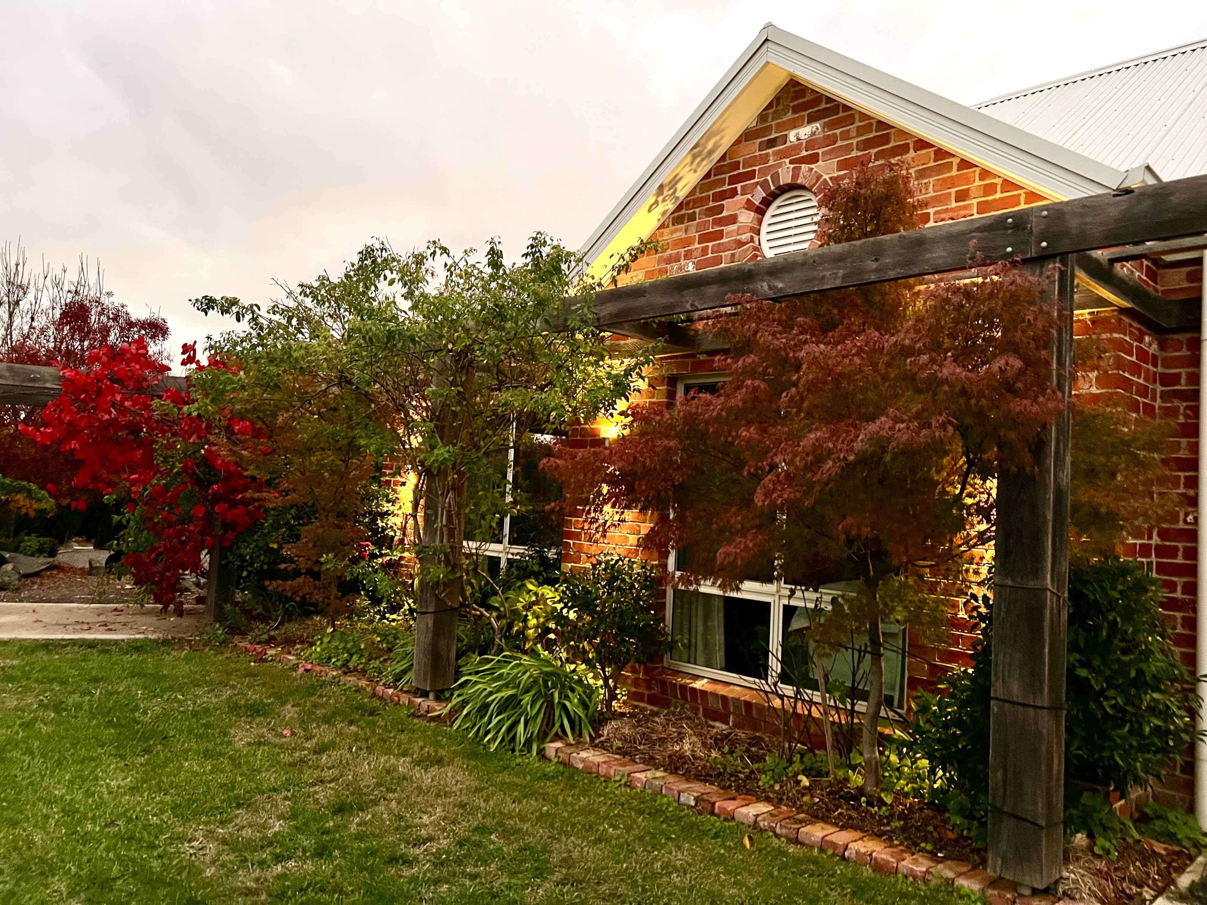 A brick house is framed by green and red foliage along with wooden trellises in a landscaped yard.