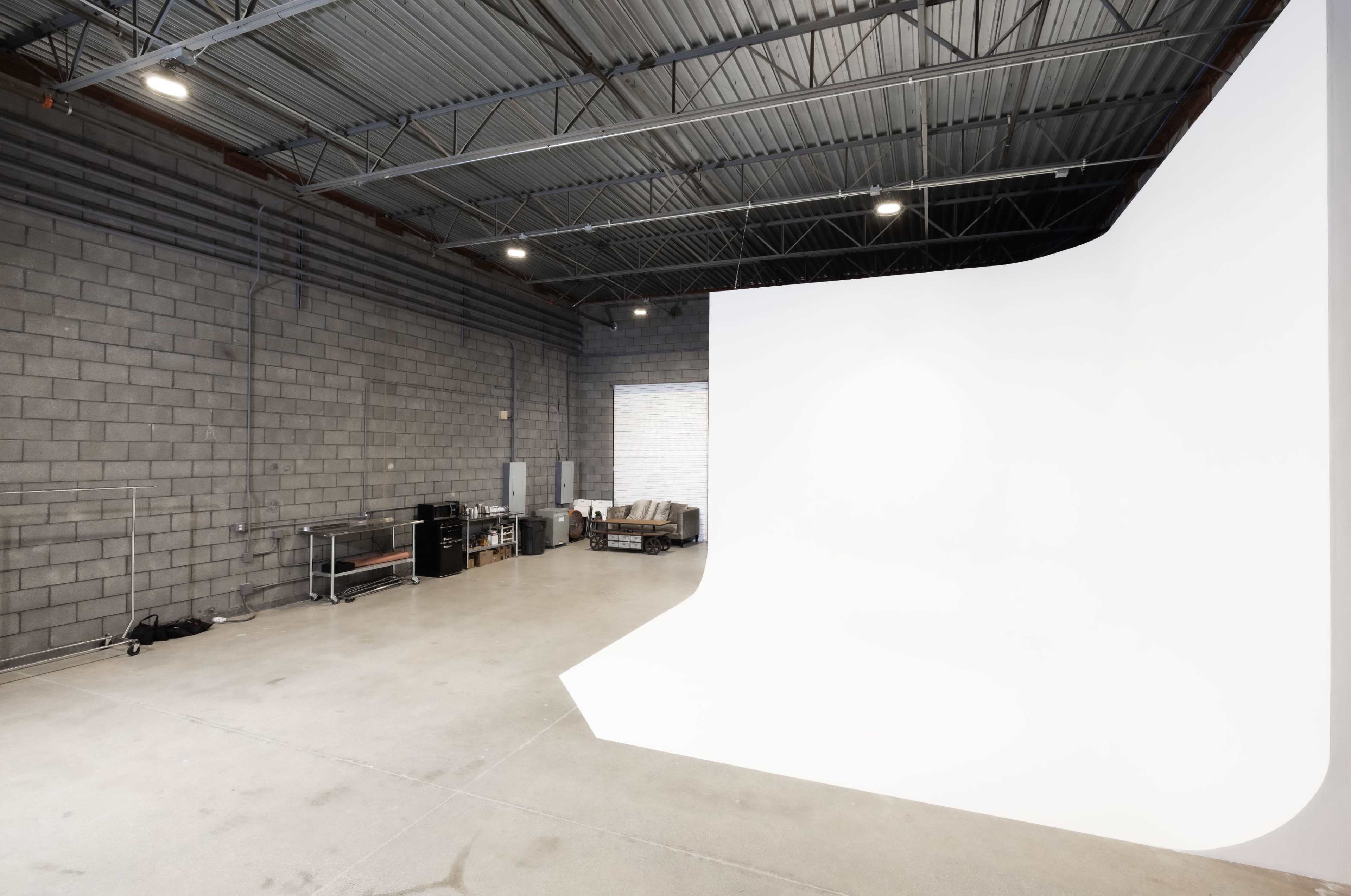 A spacious photography studio with a large white backdrop and a gray concrete wall.