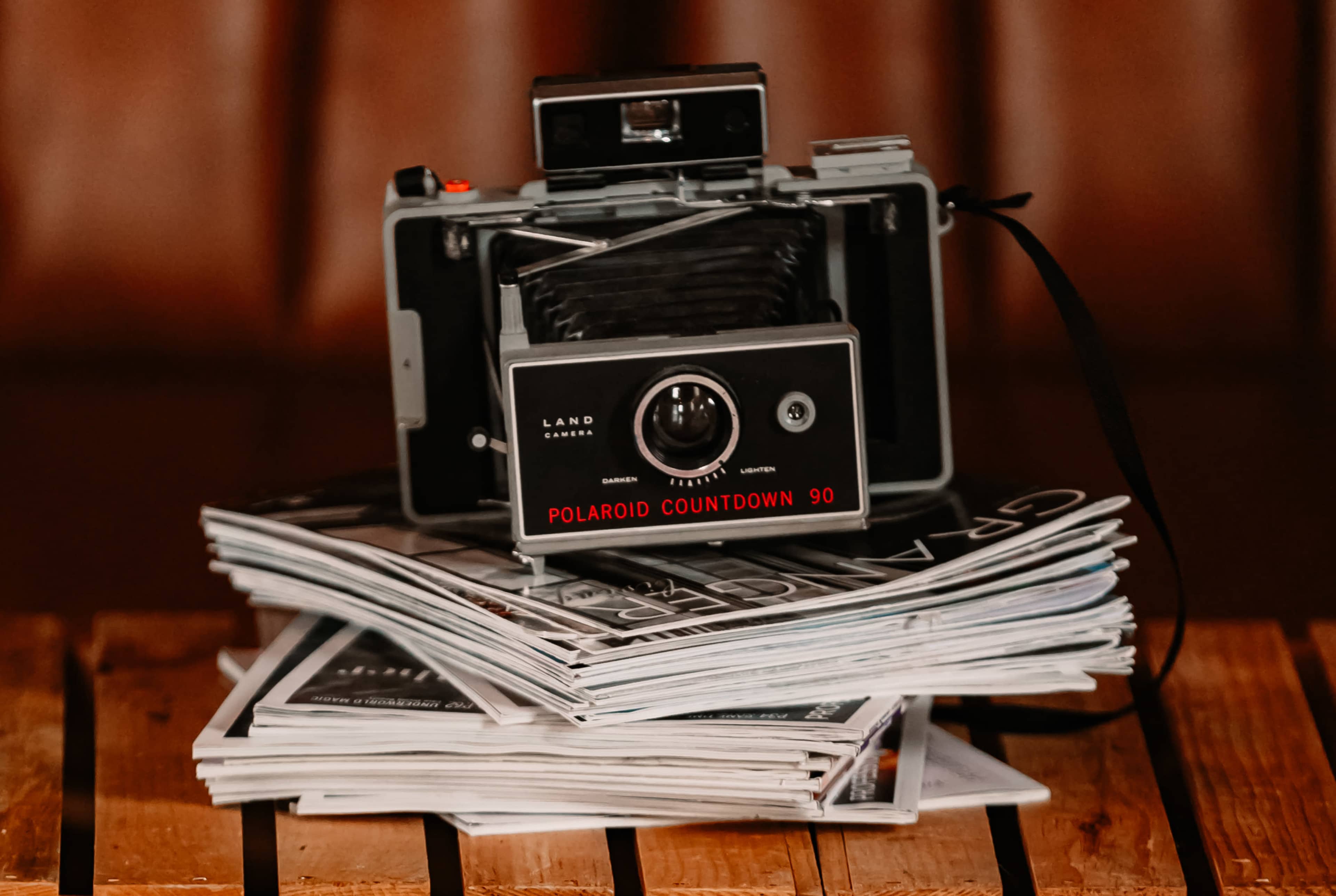 A Polaroid camera is placed on top of a stack of magazines on a wooden surface.