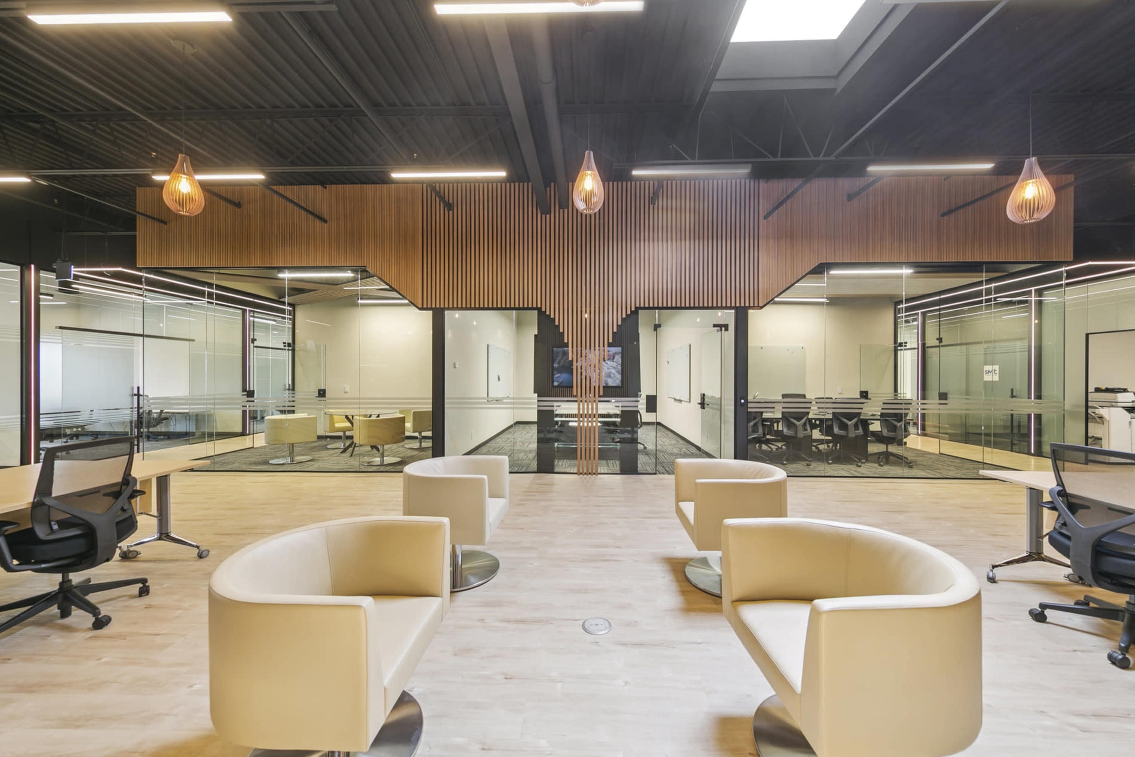 The image shows a modern office interior with beige seating, glass-walled conference rooms, and wooden accents on the walls.