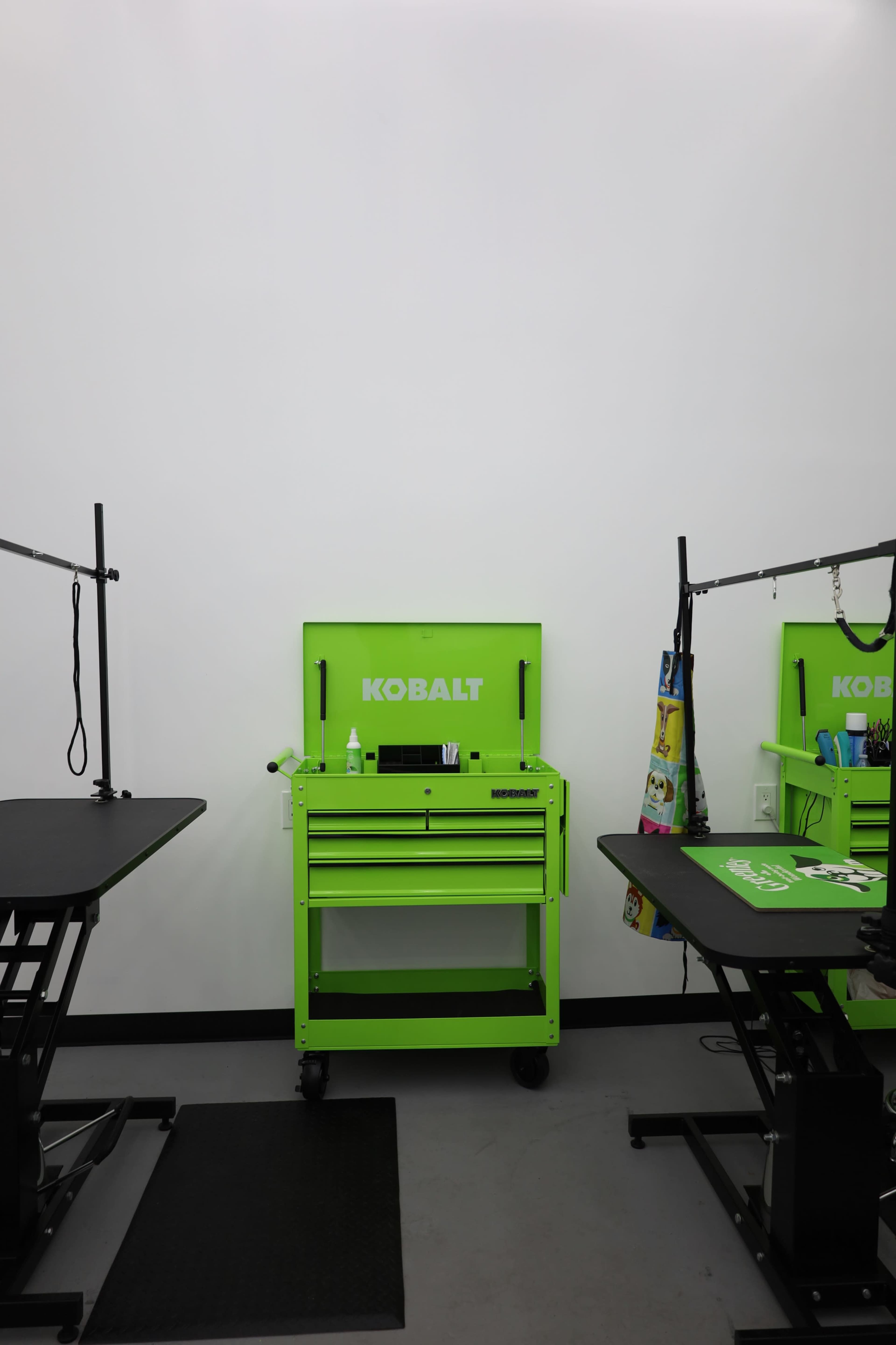 The image shows a workspace featuring a green Kobalt tool chest flanked by two black worktables with adjustable height.