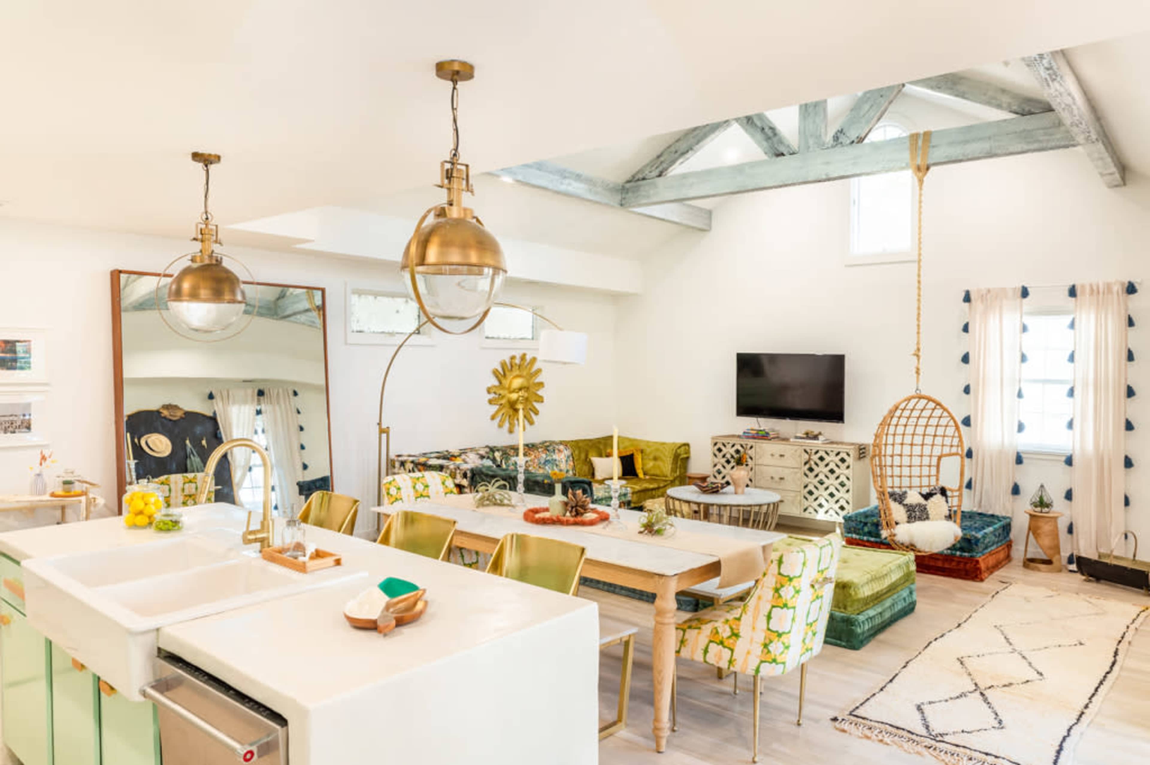 A bright, open-concept living and dining area features a modern kitchen, a large dining table, colorful seating, and decorative elements.