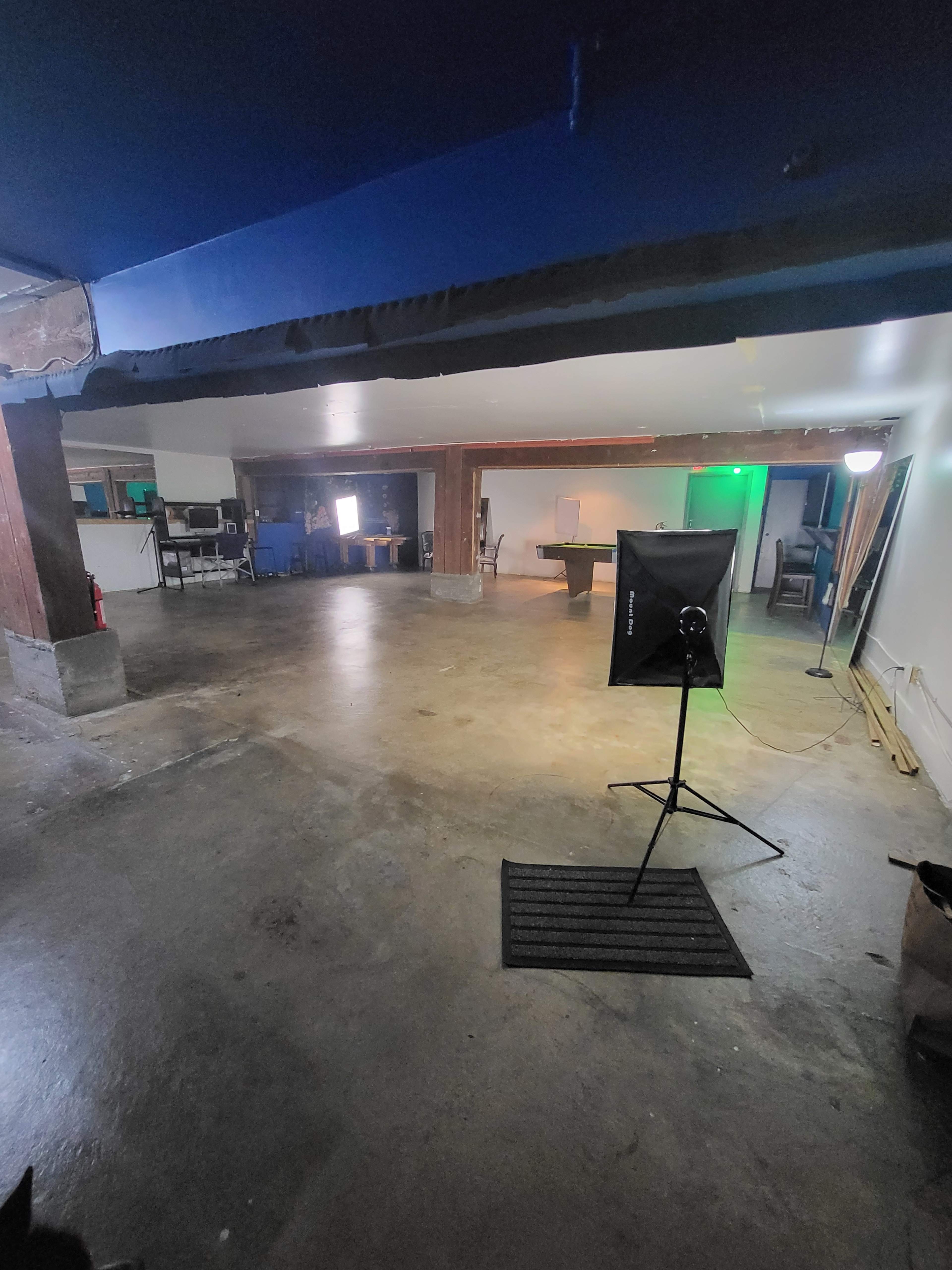 A spacious, empty room with polished concrete floors, wooden beams, and several pieces of furniture visible in the background.