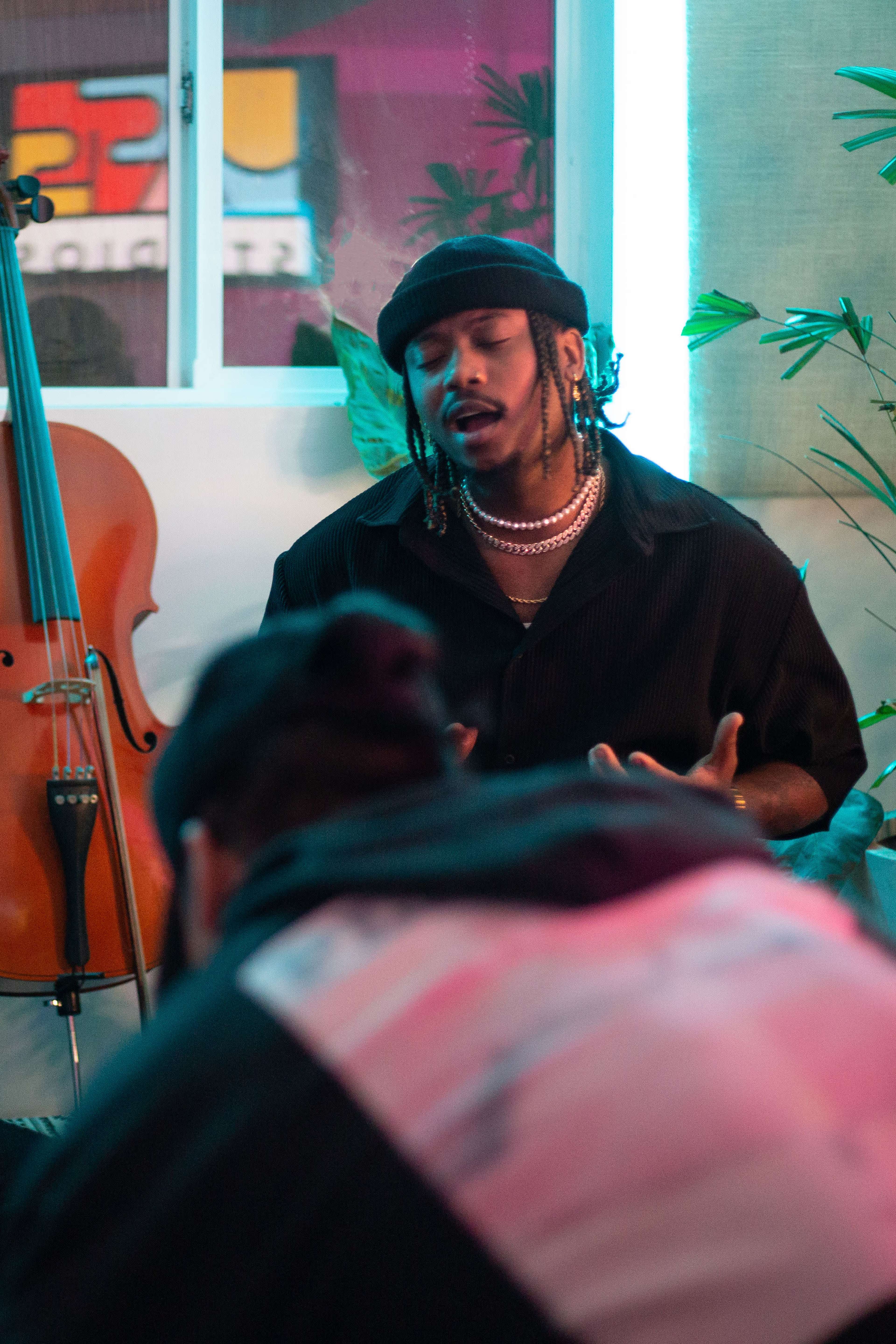 A musician sits with a cello visible nearby, engaged in a conversation with another person out of view.