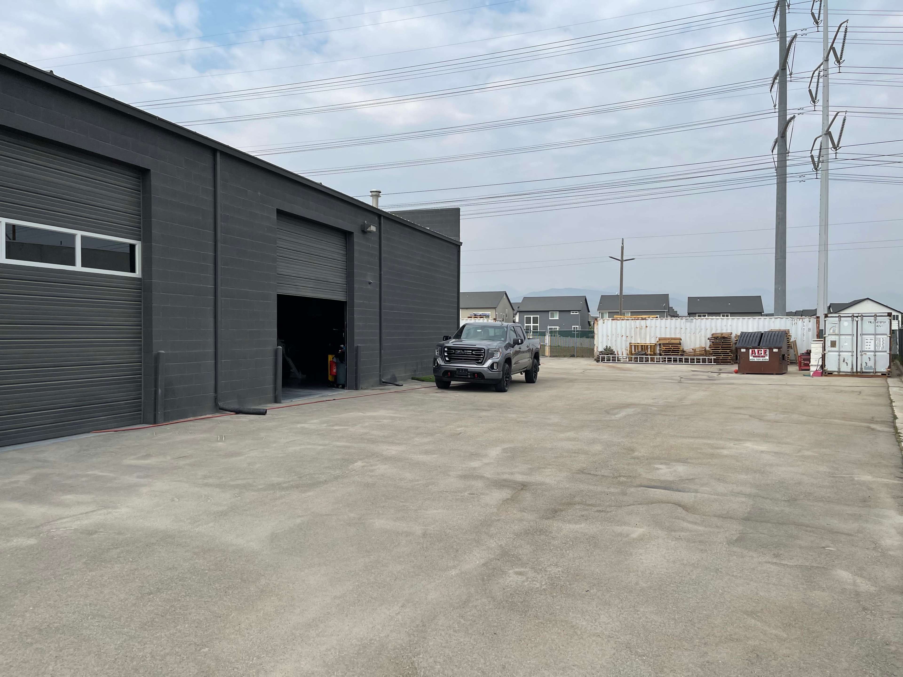 A black truck is parked in front of a gray industrial building with large rolling doors on a paved outdoor area.