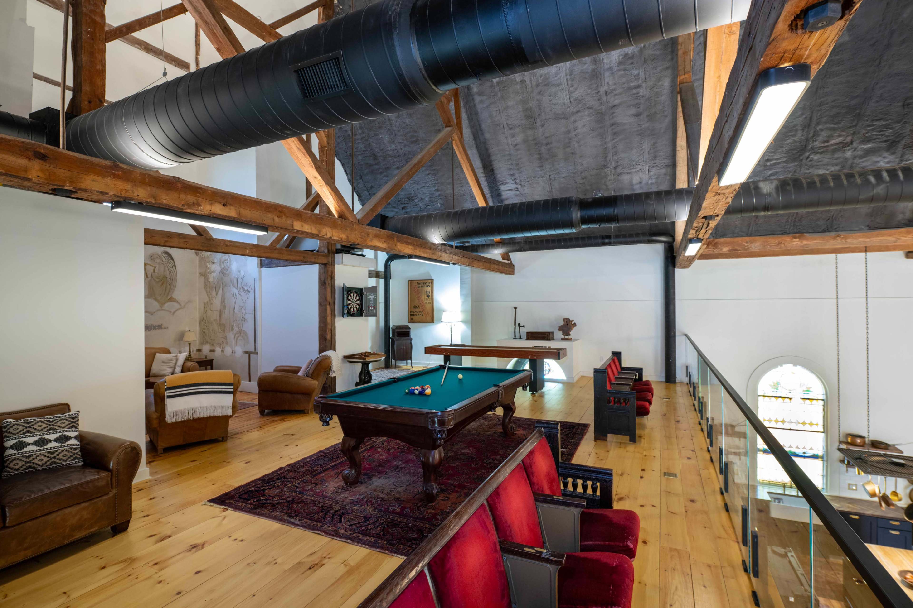 The image shows a spacious loft area with wooden beams, a pool table, and seating arranged in a cozy layout.