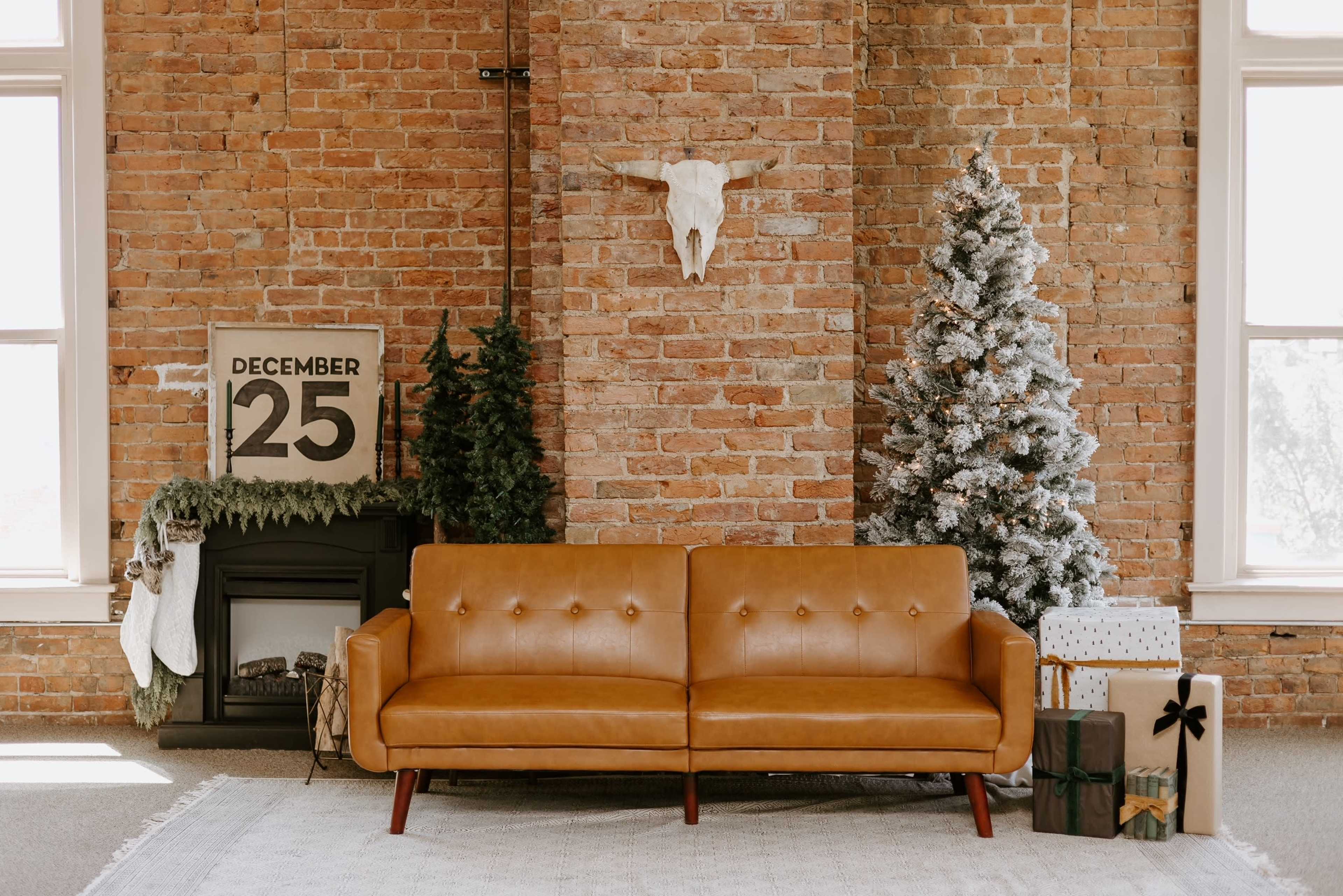 The image features a brown leather sofa in front of a brick wall, with a decorated Christmas tree, a fireplace, and a sign displaying "DECEMBER 25" nearby.